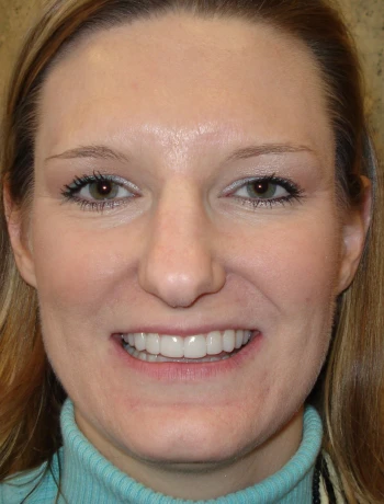Close-up portrait of a woman with long light brown hair, smiling and wearing a light blue turtleneck sweater.