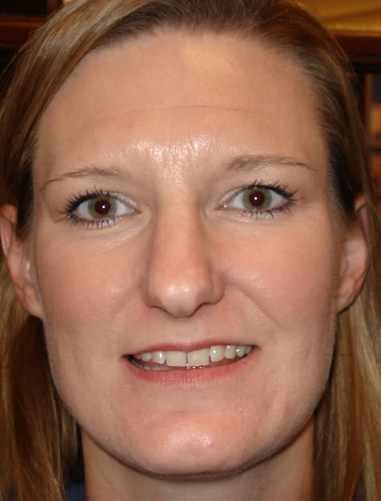 Close-up of a woman with light brown hair smiling gently, showing her teeth.