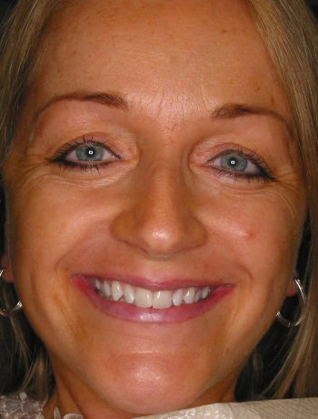 Close-up of a smiling woman with blue eyes, light brown hair, and silver hoop earrings.
