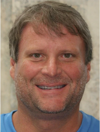 Smiling middle-aged man with short brown hair and light facial stubble wearing a blue shirt.
