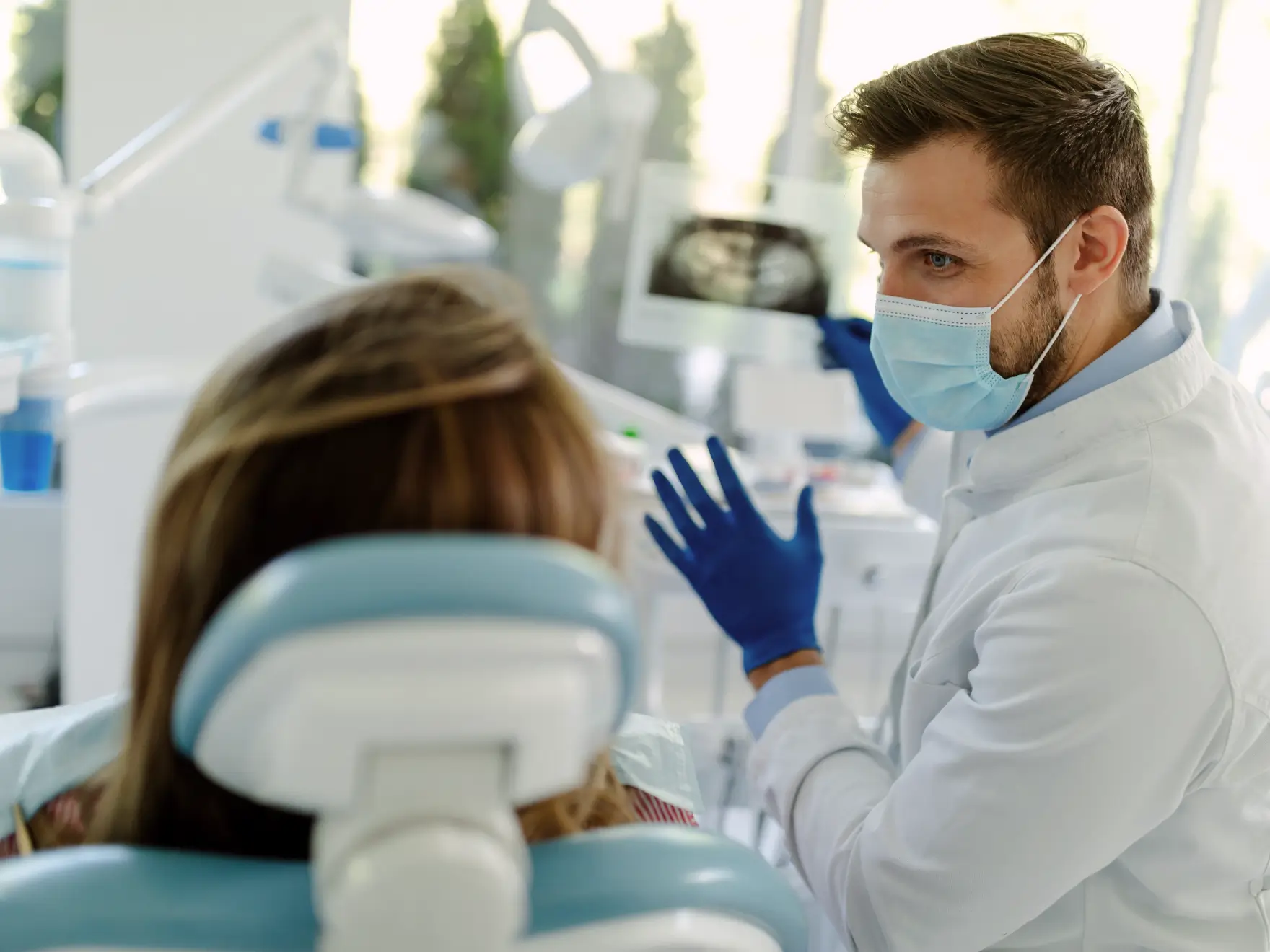 Dentist wearing a mask and gloves showing a dental x-ray to a patient seated in a dental chair.