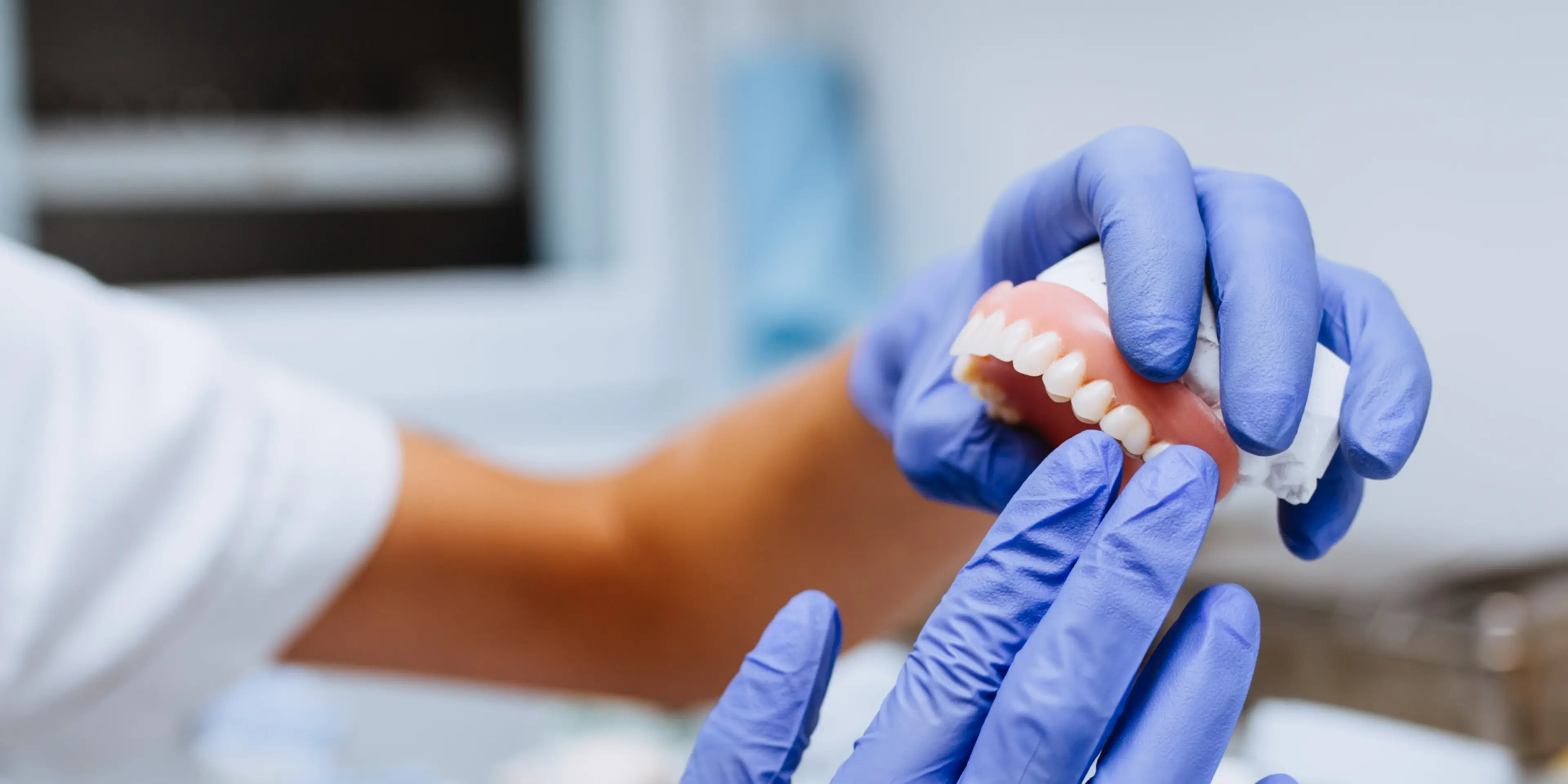 Gloved hands holding and inspecting a dental model with artificial teeth and gums.