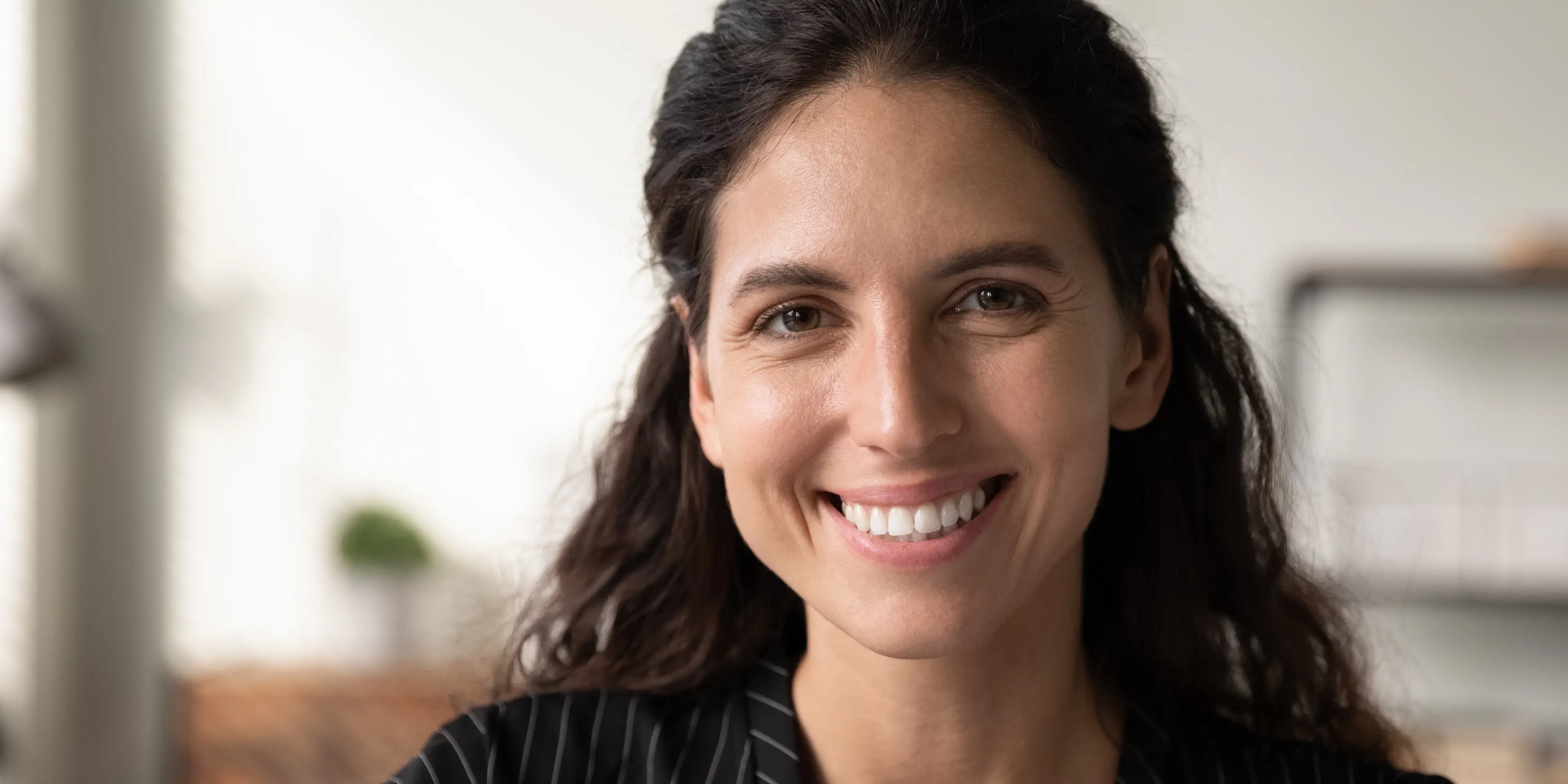 Close-up of a smiling woman with dark hair in a softly lit room.