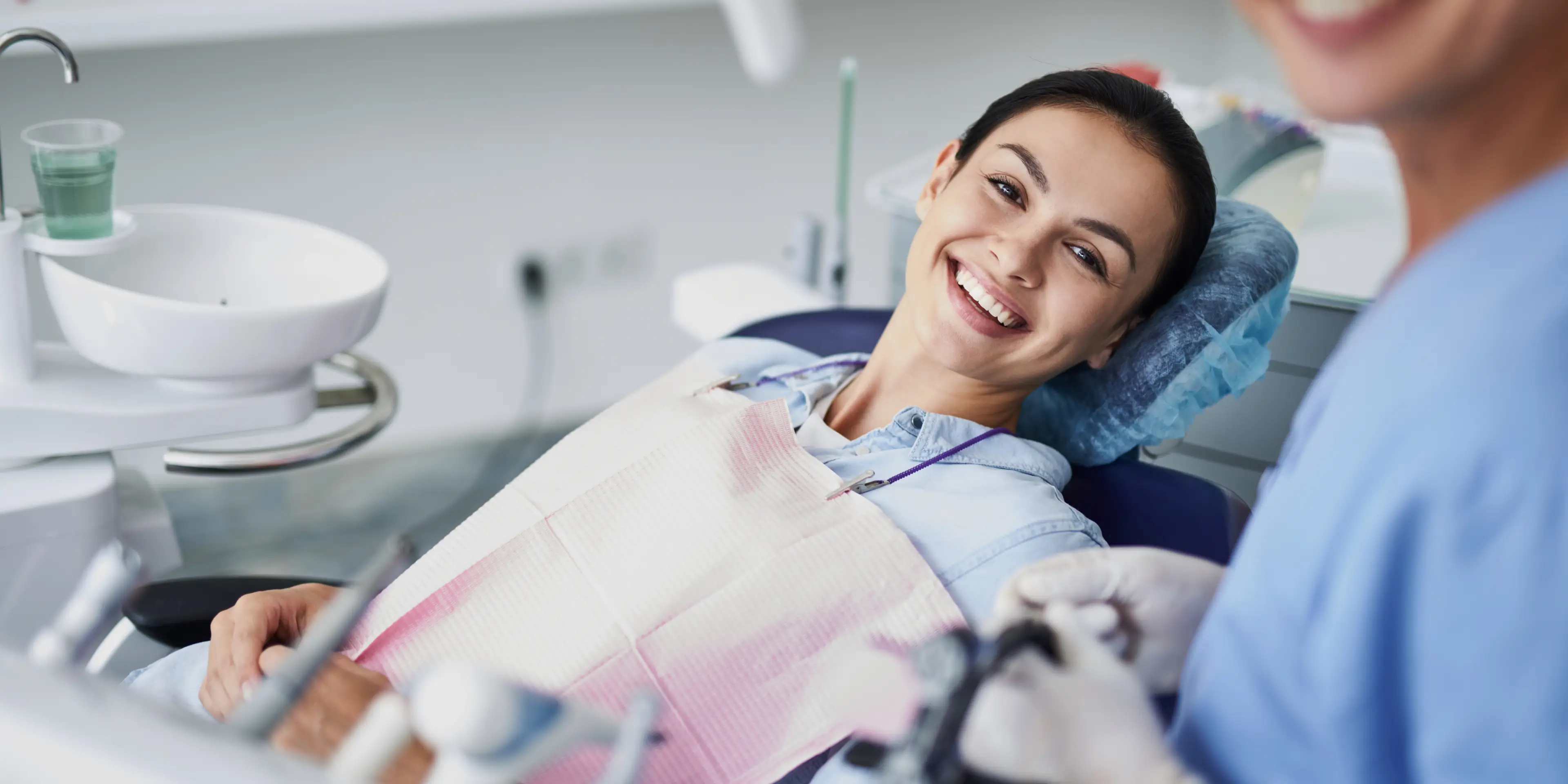 Smiling woman reclined in a dental chair with a bib, ready for dental treatment.
