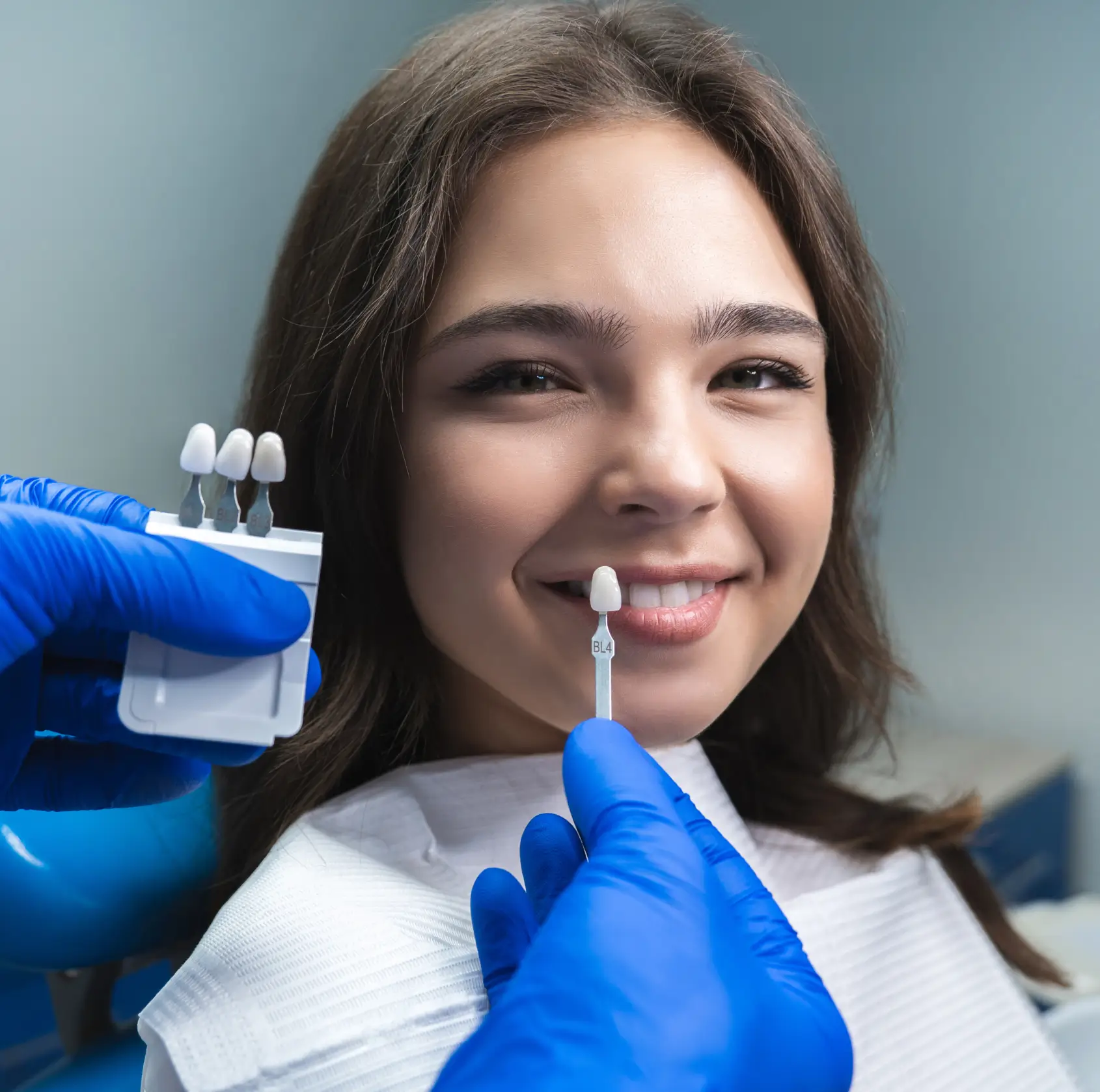 Dental professional matching a dental veneer shade to a smiling woman's teeth.