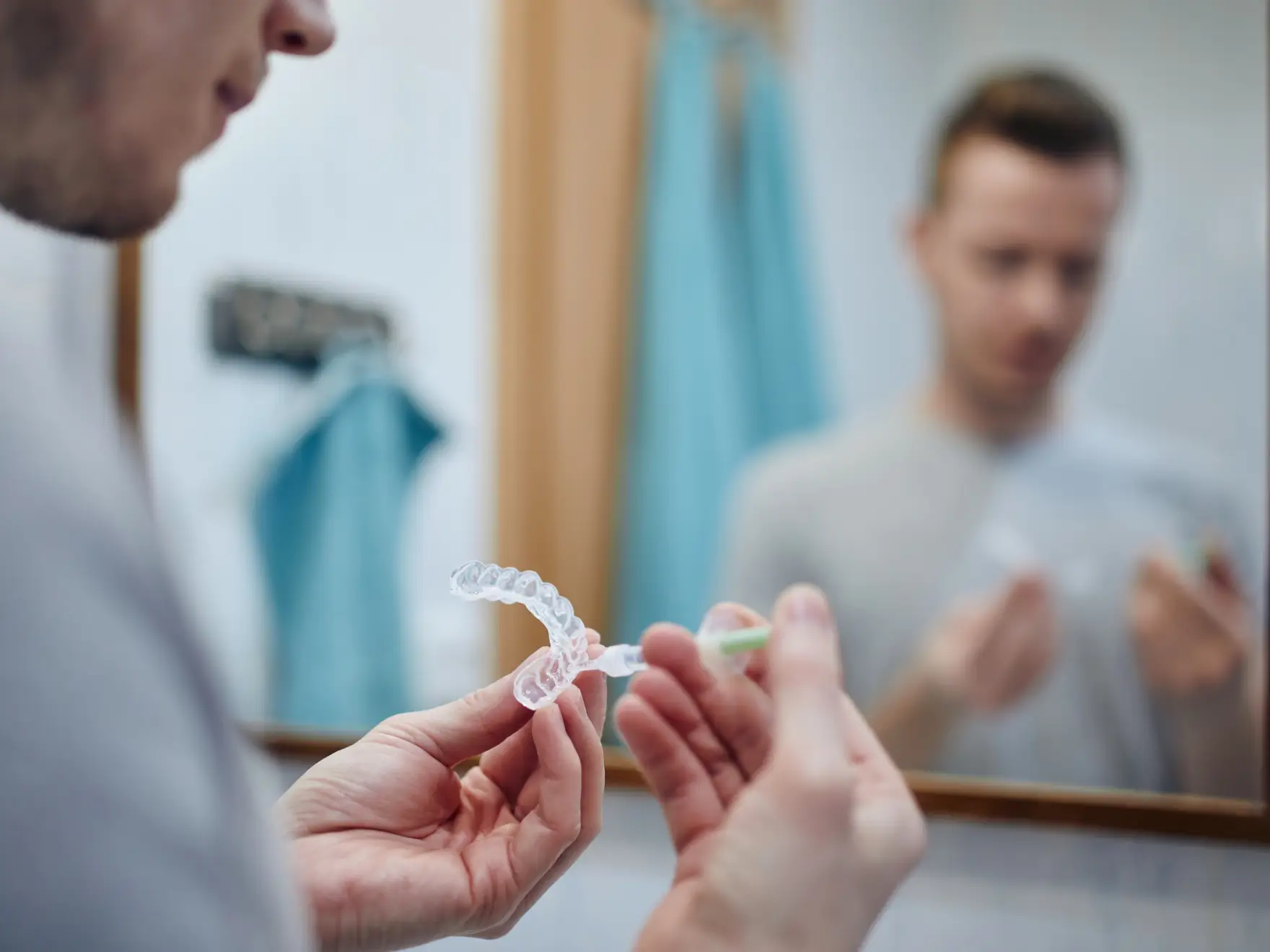 Man applying whitening gel to a clear dental aligner in front of a bathroom mirror.