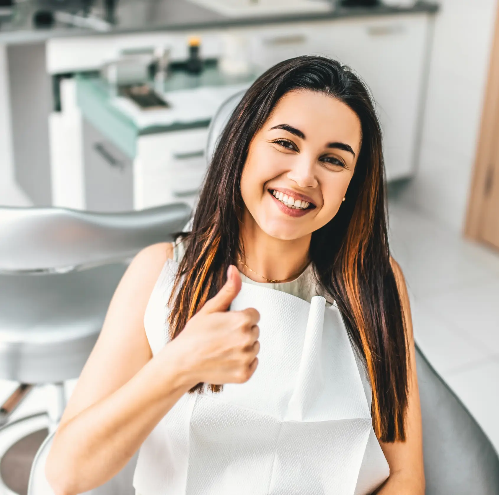 Smiling woman in a dental office giving a thumbs-up gesture.