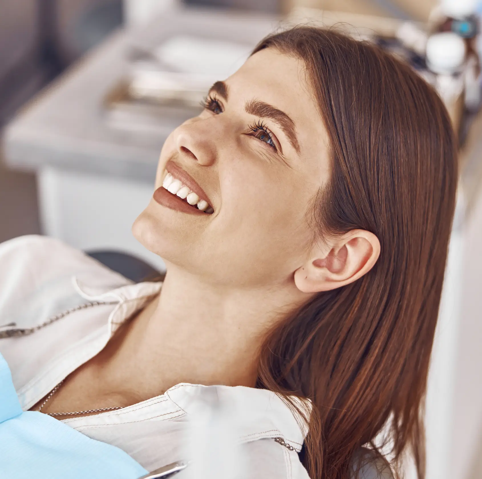 Smiling young woman reclining, wearing a dental bib in a dental clinic setting.
