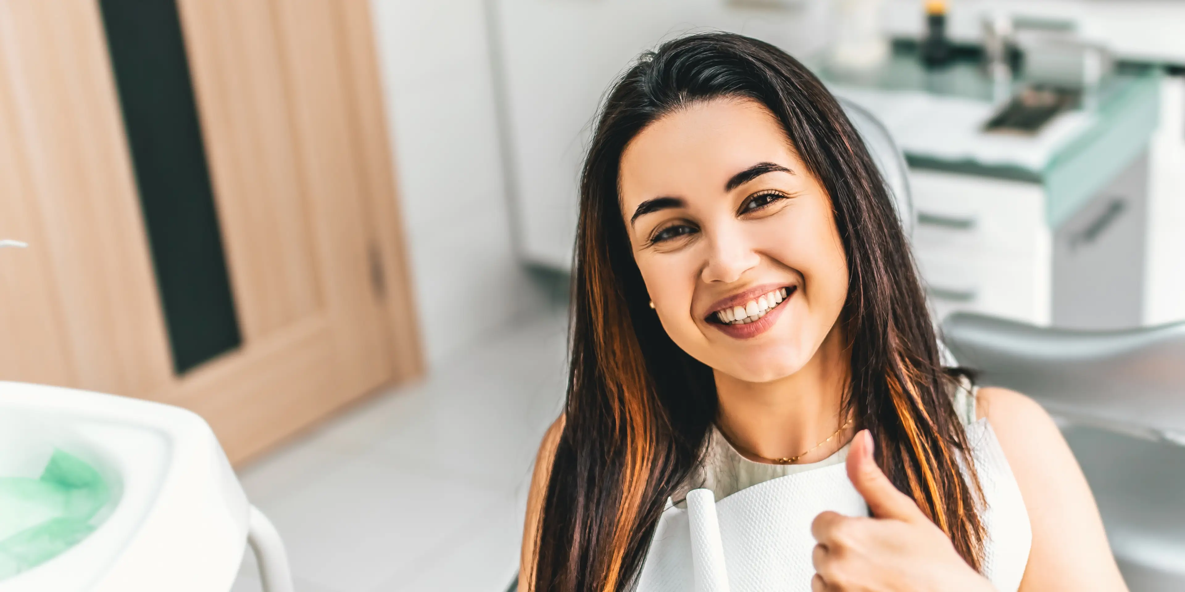Smiling woman sitting in a dental chair giving a thumbs up in a dental office.