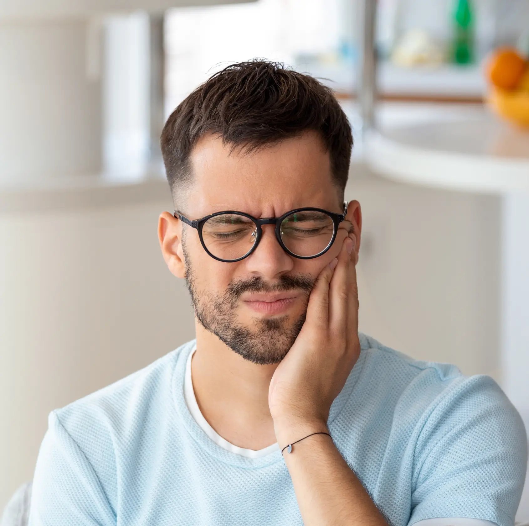 Man wearing glasses with eyes closed, holding his cheek in pain, indicating a toothache.
