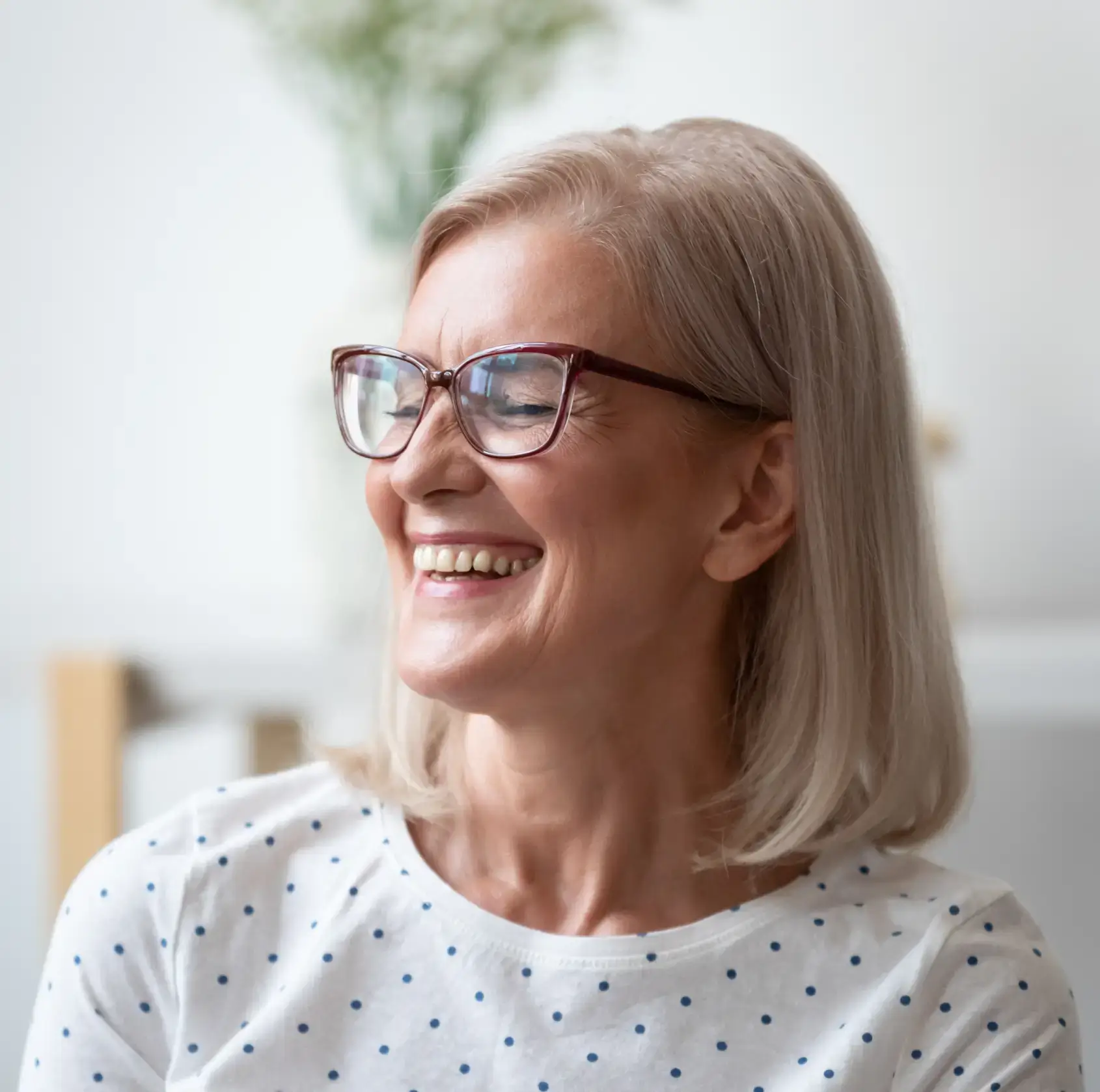 Smiling middle-aged woman with glasses and a white polka dot shirt looking to the side.