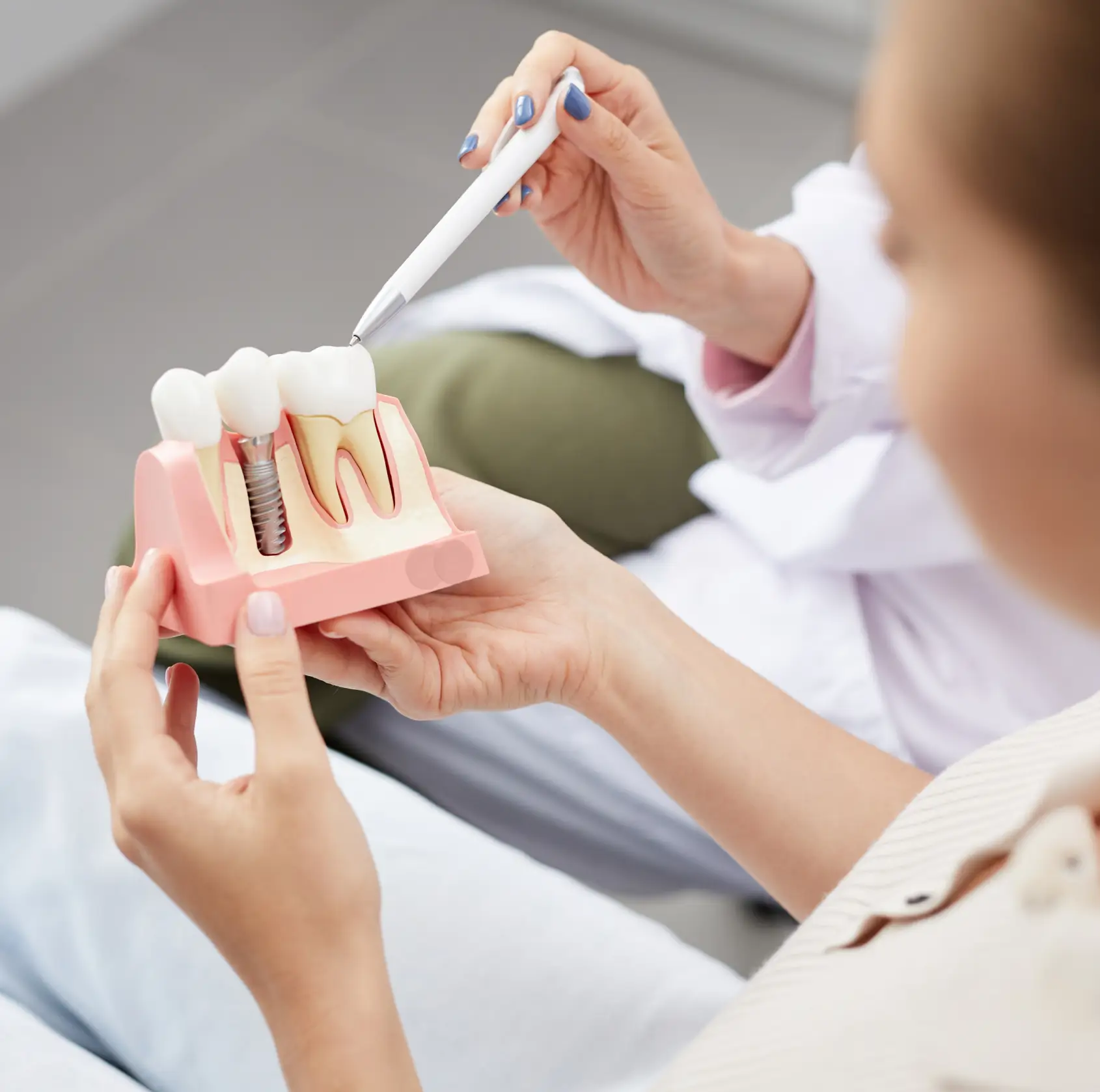 Dentist holding a dental implant model and pointing at it with a pen during consultation.