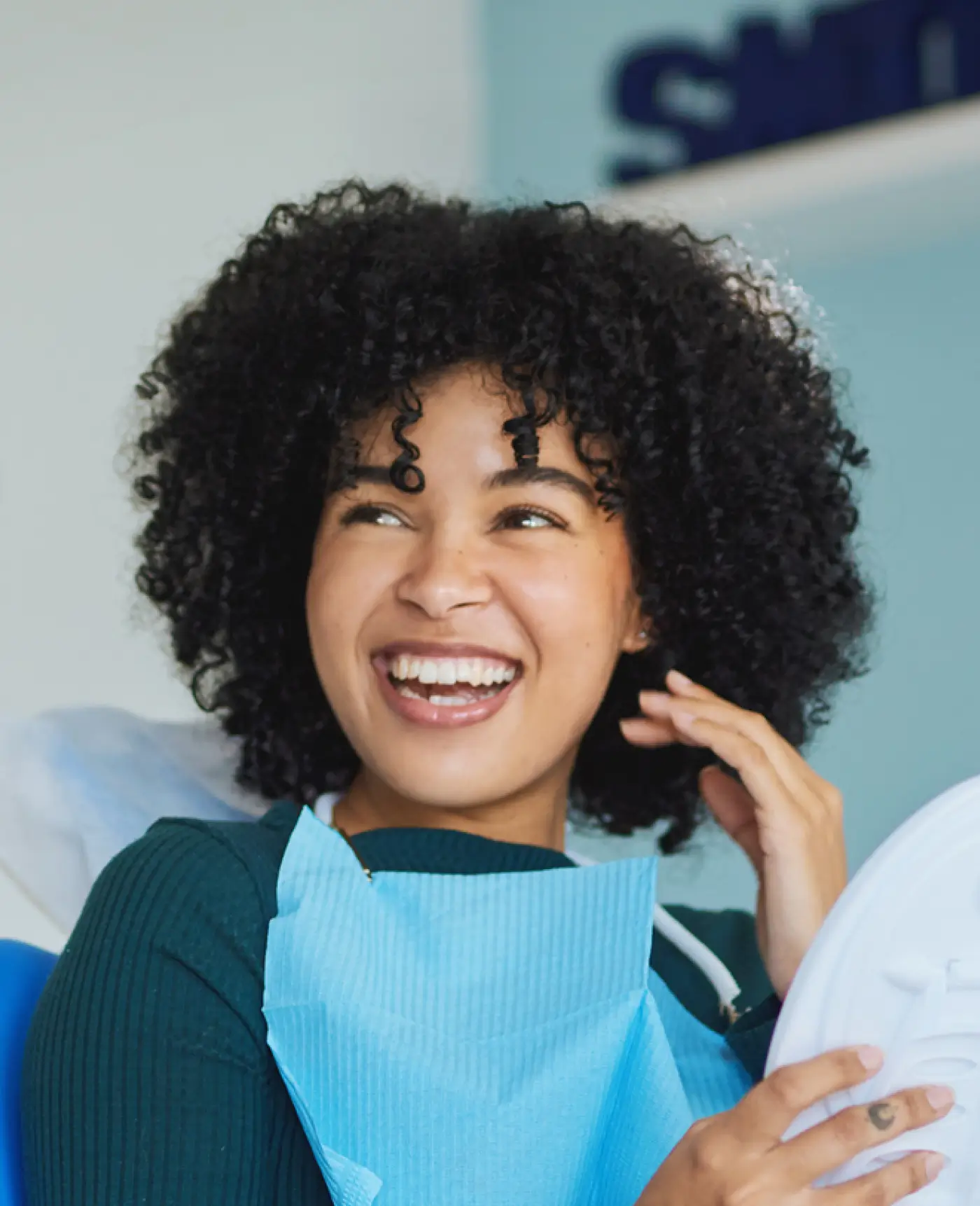 Smiling woman with curly hair wearing a dental bib and holding a dental mirror.