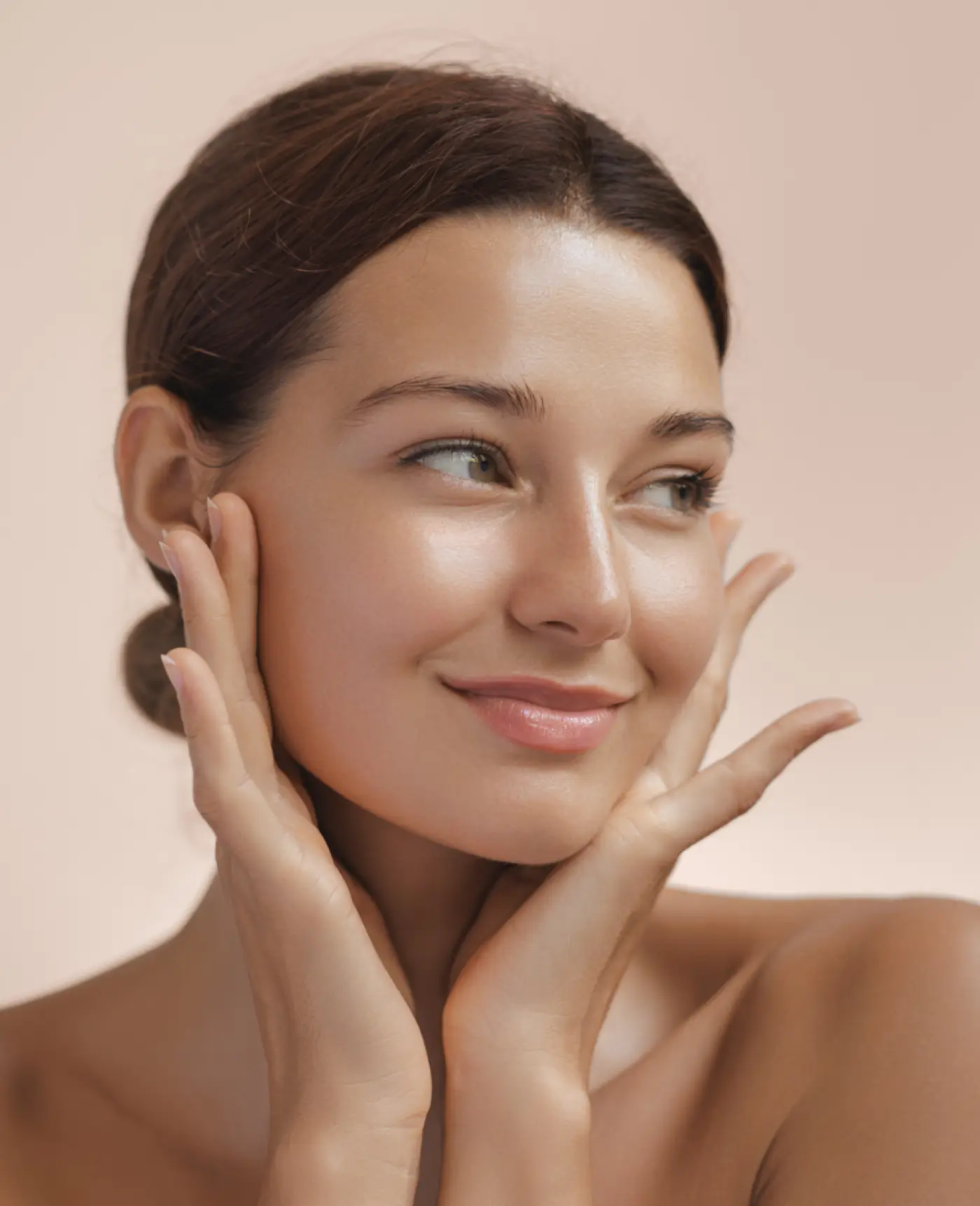 Smiling woman with clear skin gently touching her face against a light beige background.
