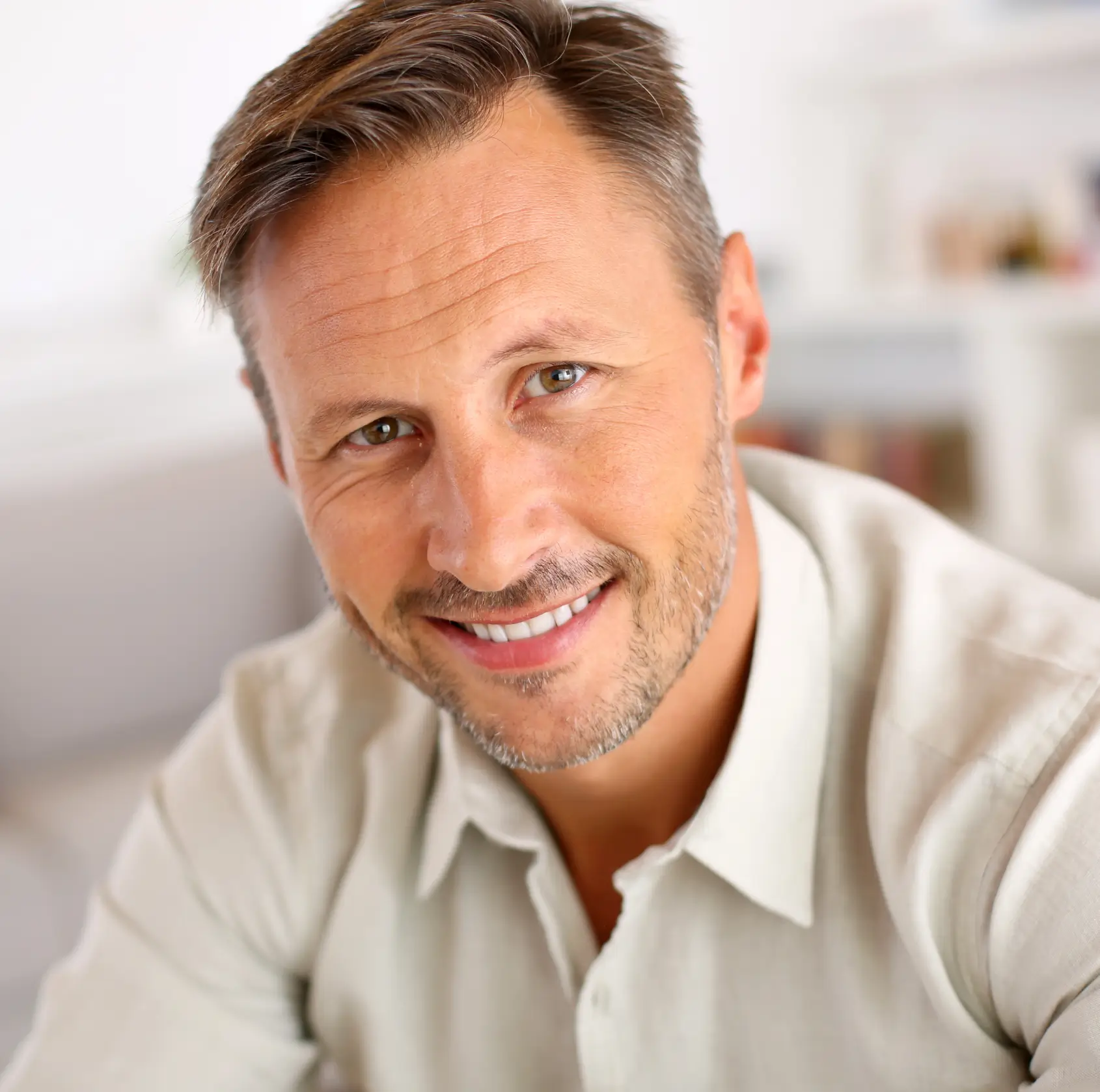 Smiling middle-aged man with short brown hair and light stubble wearing a light-colored shirt.