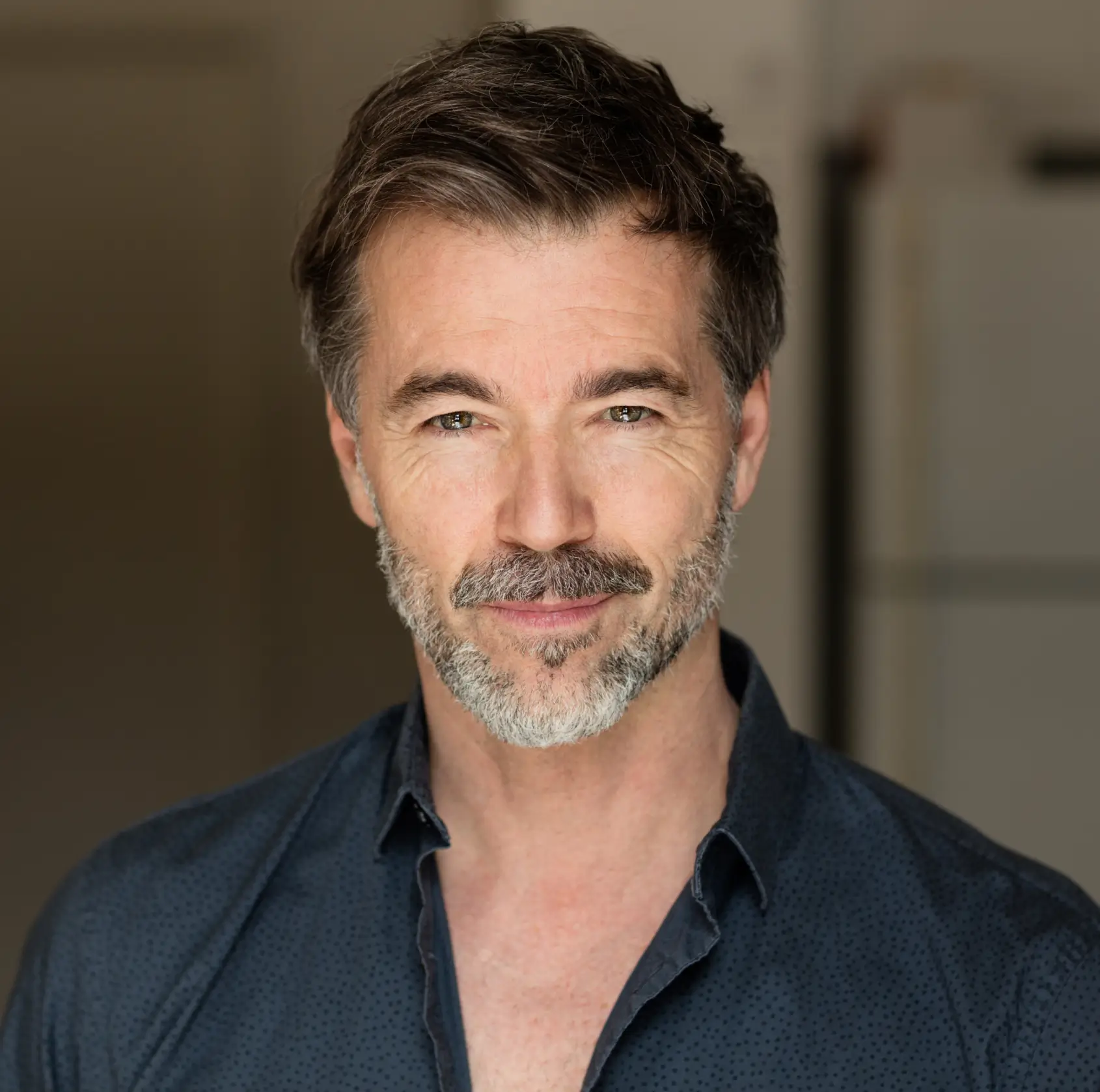 Middle-aged man with salt-and-pepper beard and hair, wearing a dark blue shirt, smiling softly at the camera.