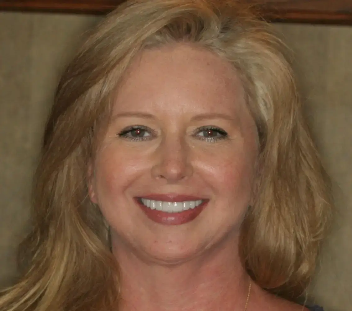 Close-up of a smiling middle-aged woman with blonde hair and light makeup.