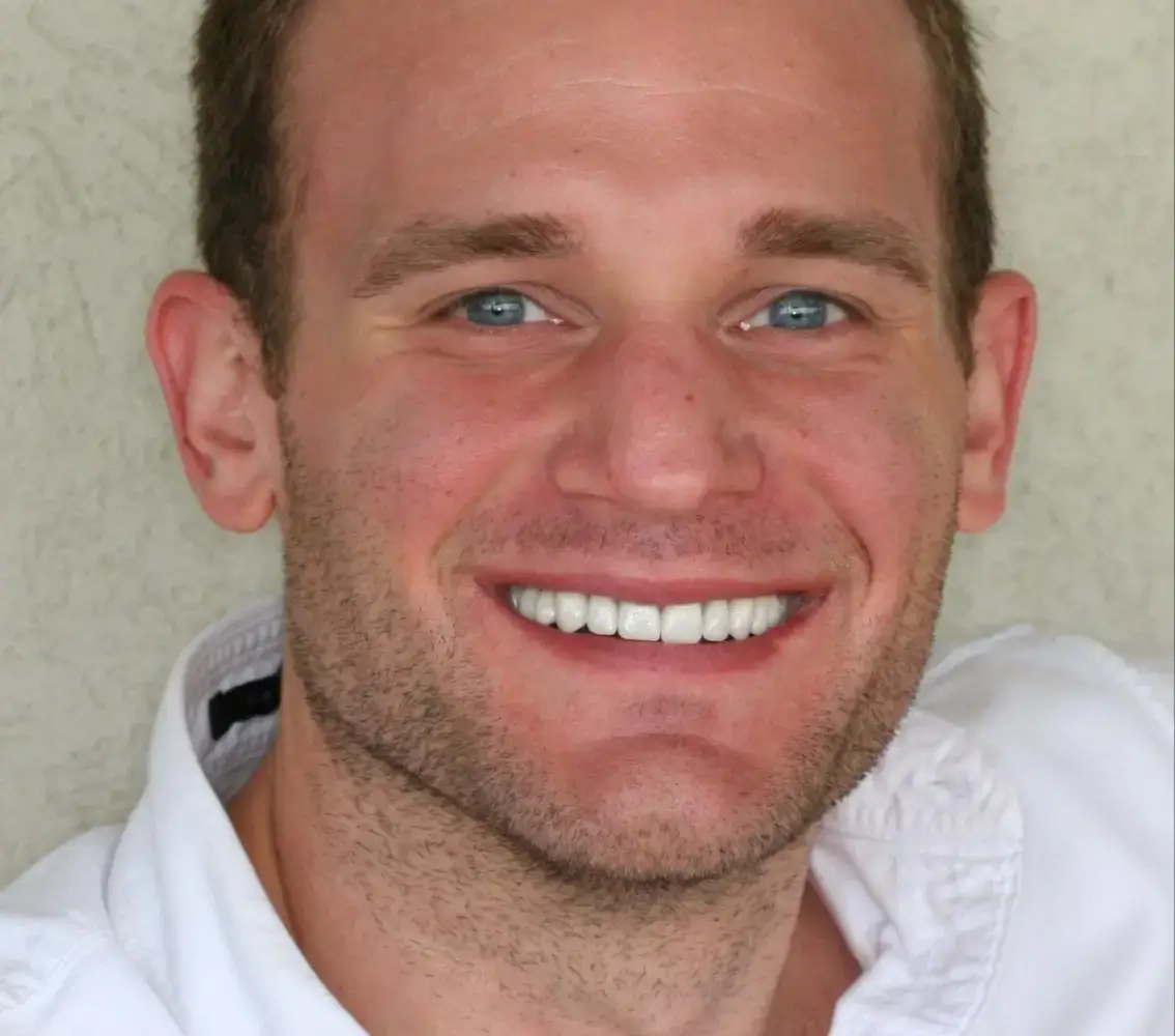 Close-up of a smiling man with blue eyes and short hair wearing a white shirt.