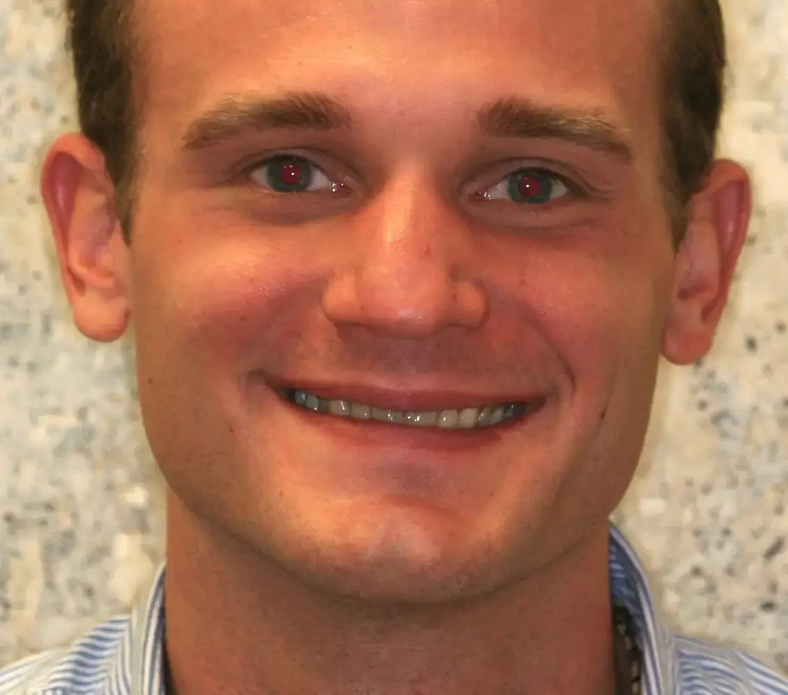 Close-up of a smiling young man with short brown hair and light skin, wearing a striped shirt.