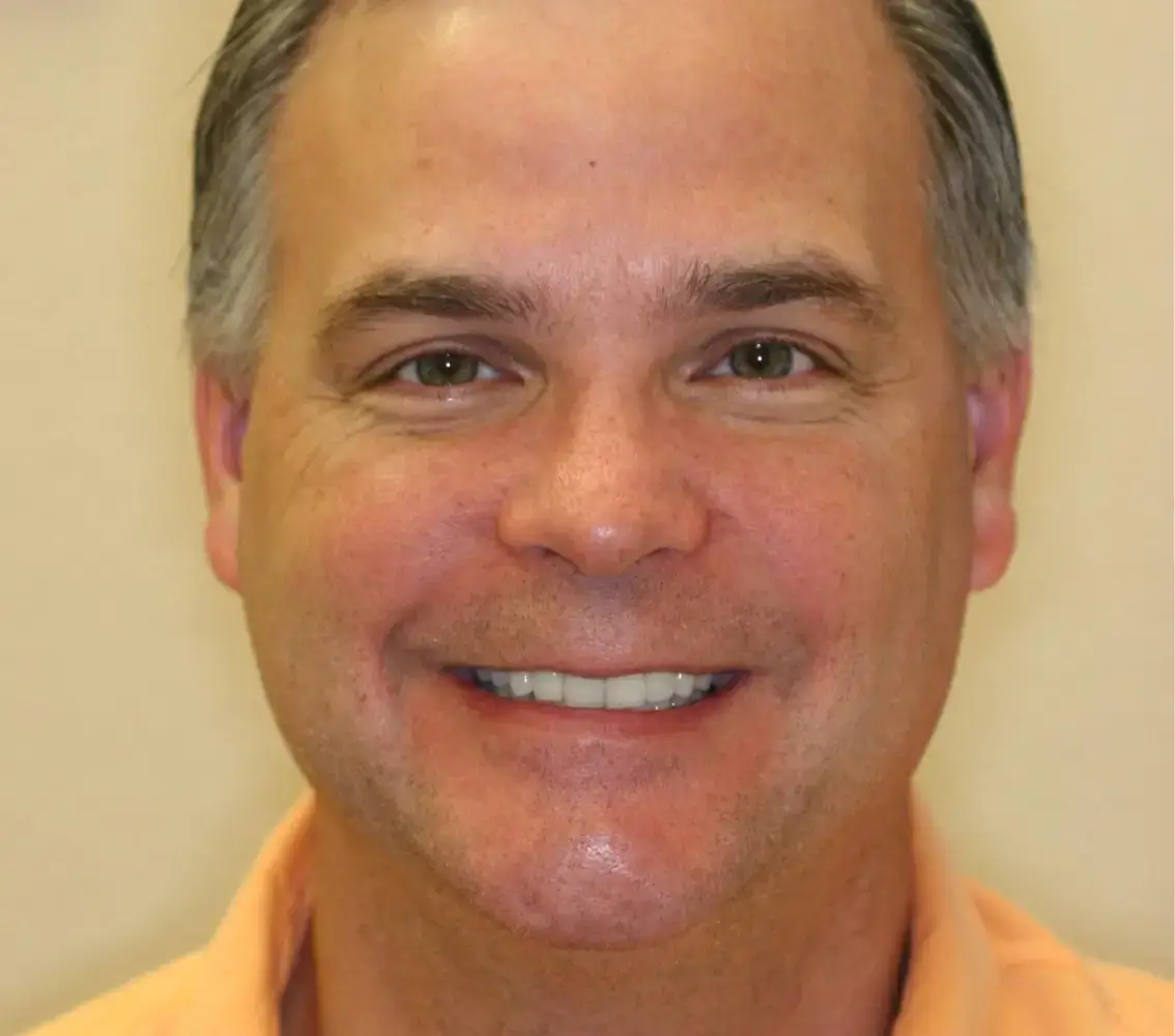 Close-up of a middle-aged man smiling with short gray hair and wearing a light orange shirt.