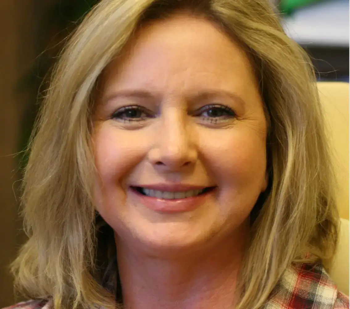 Smiling middle-aged woman with blonde hair wearing a plaid shirt.