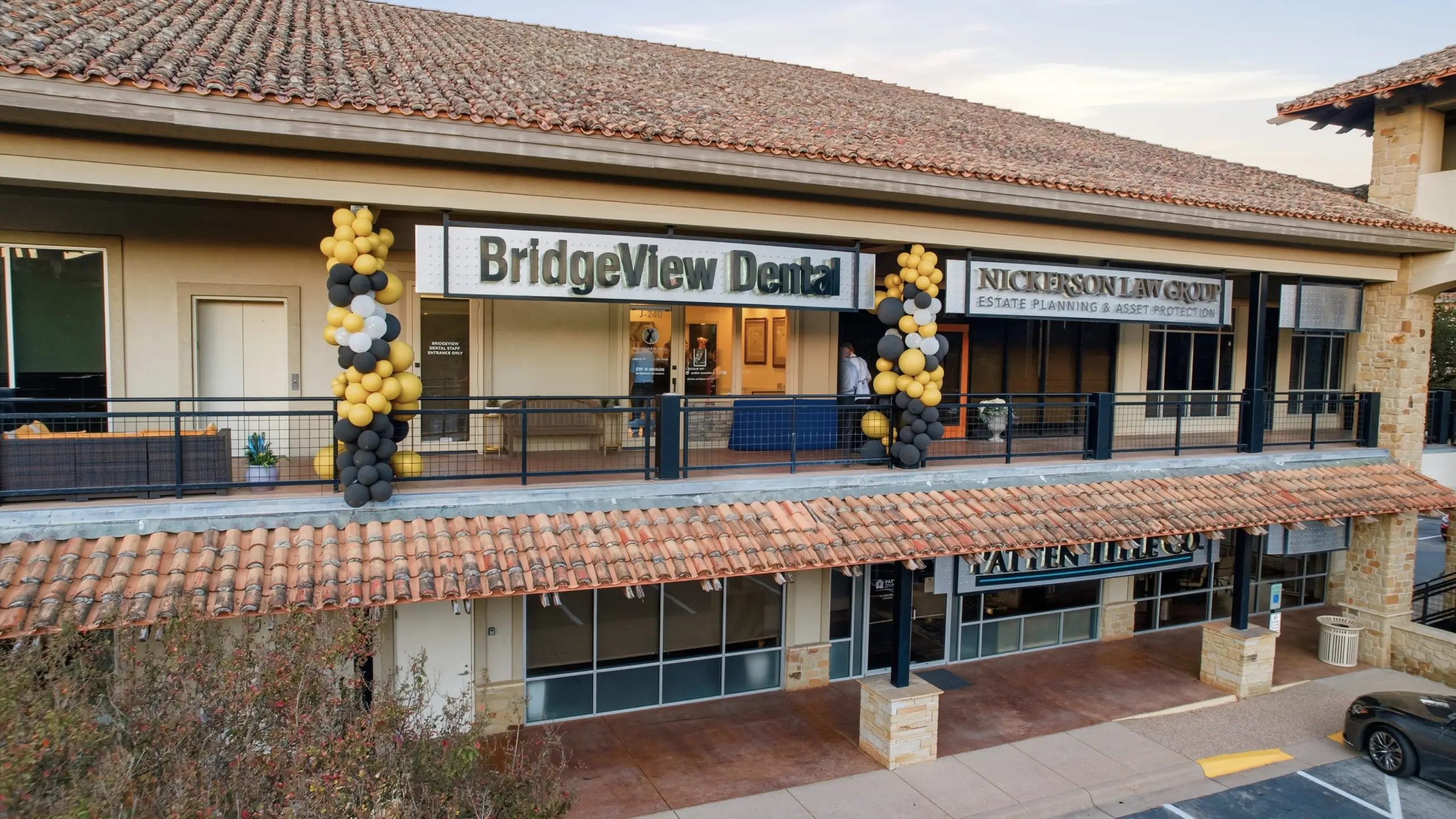 Exterior view of a two-story building with signs for BridgeView Dental and Nickerson Law Group, decorated with black, gold, and white balloons.