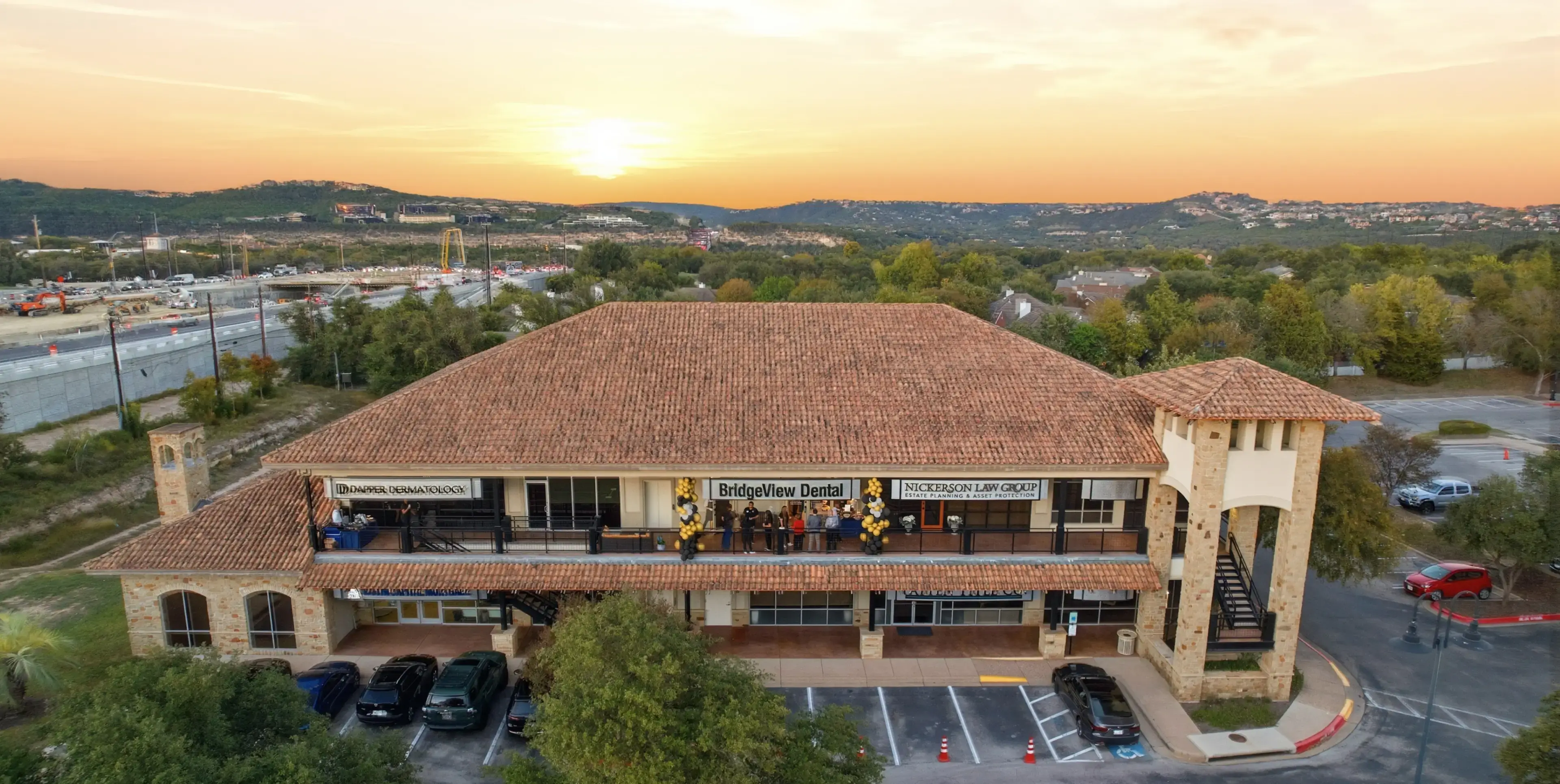 Two-story commercial building with a tiled roof at sunset, featuring signs for BridgeView Dental, Nickerson Law Group, and Dapper Dermatology, with cars parked in front.