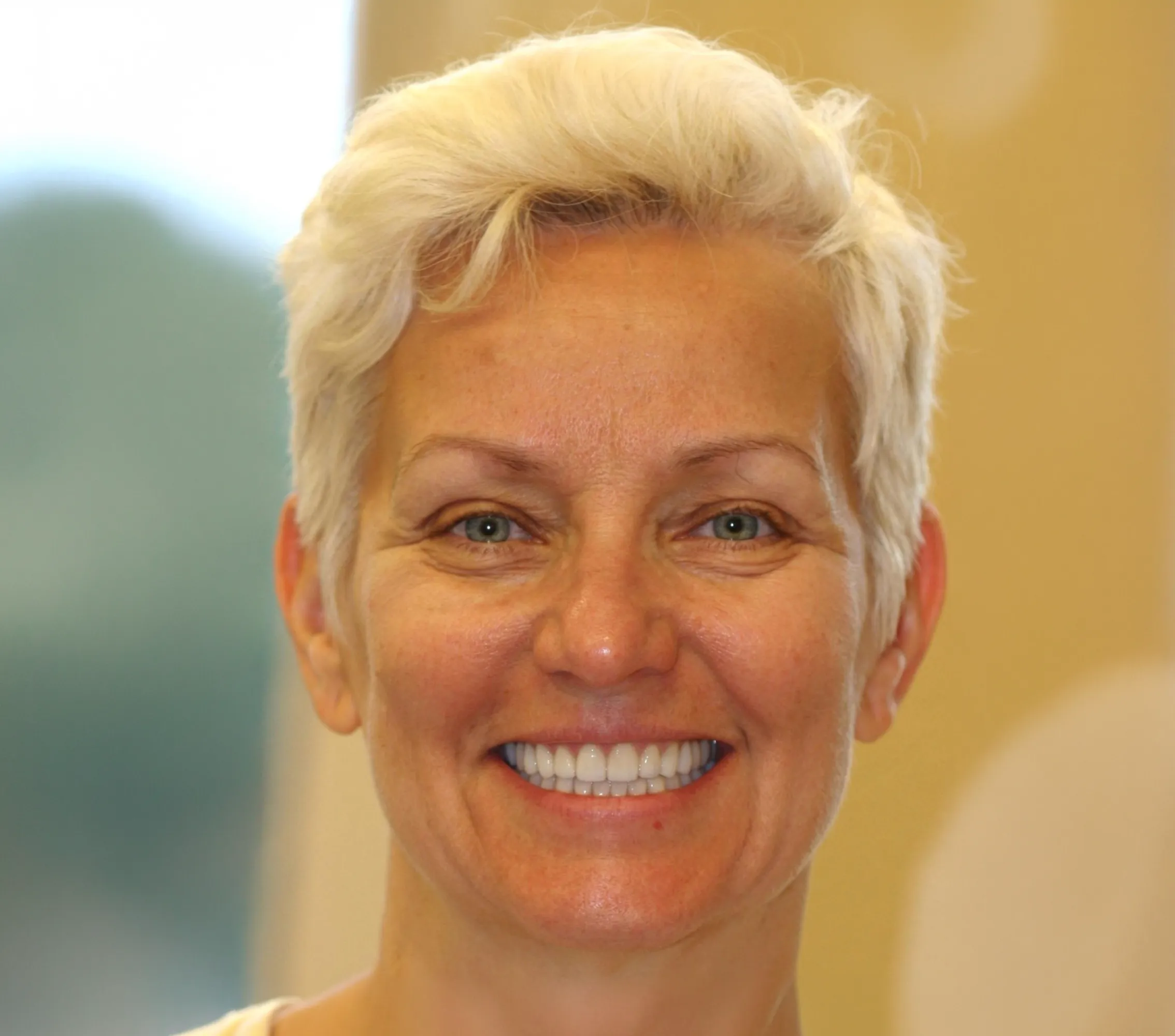 Close-up of a smiling middle-aged woman with short platinum blonde hair and blue eyes.