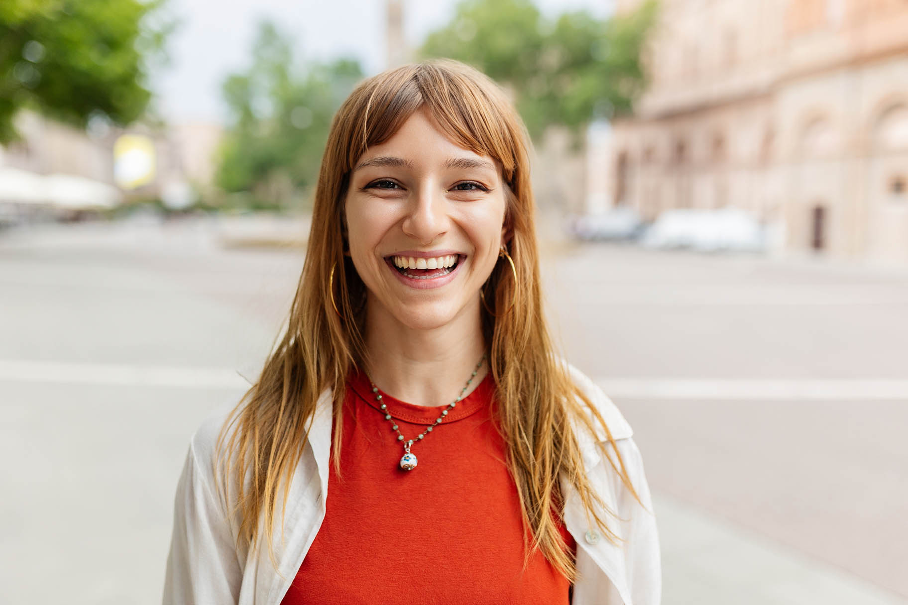 A young woman wearing an orange top is smiling at the camera.