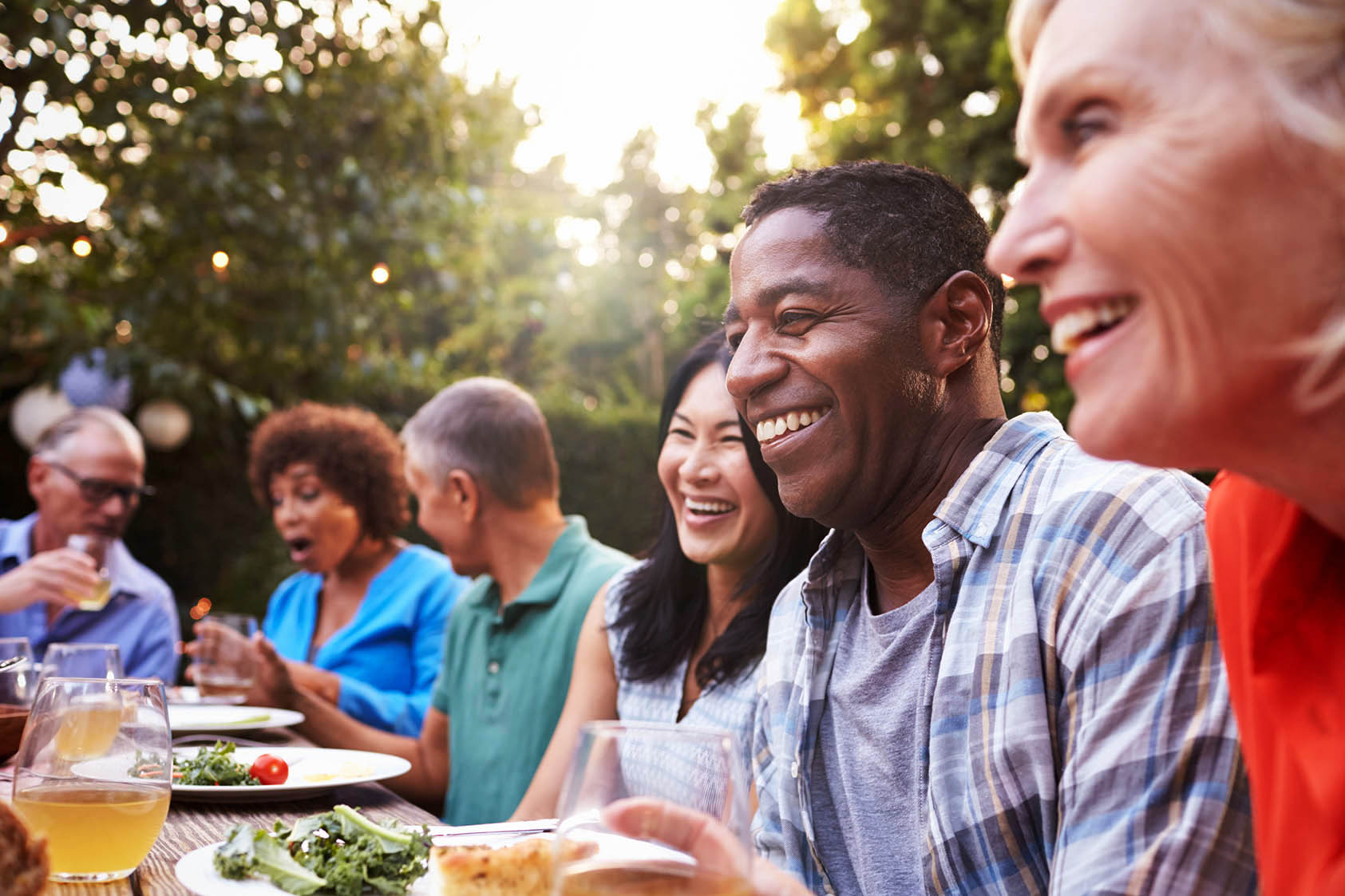 A group of diverse and mature friends enjoys retirement at an outdoor dinner party in the summer at sunset.