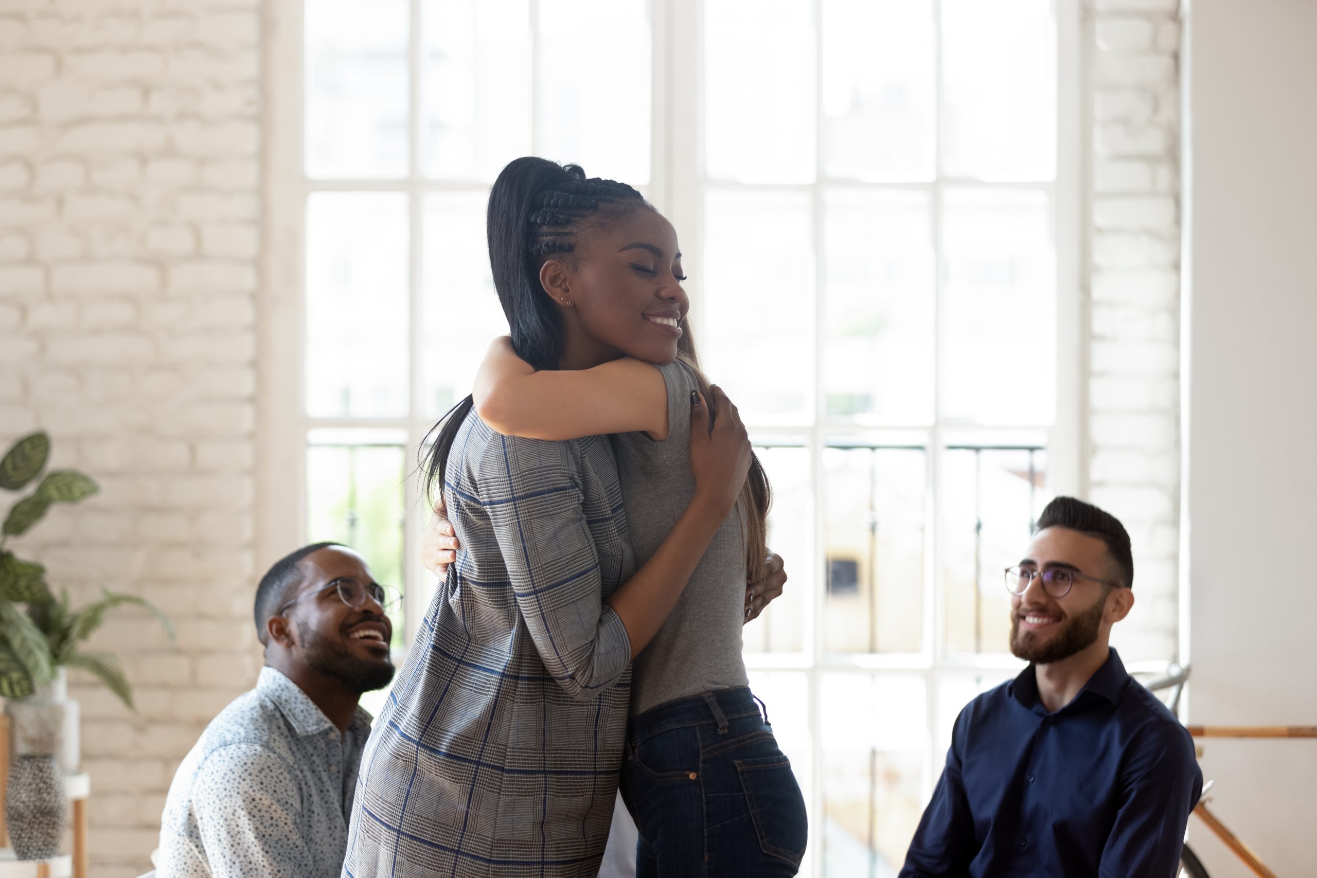 african american woman hugging a caucasian woman at an aa meeting