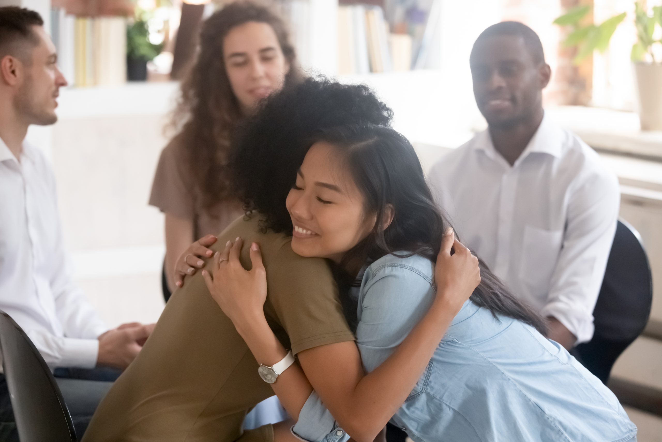 african american and asian women hugging each other for support at aa meeting