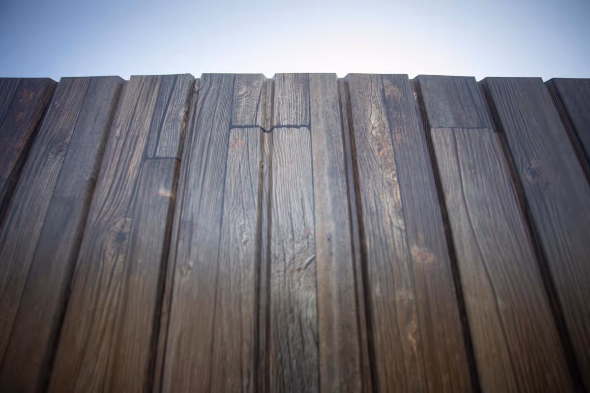 Close-up of a dark wooden fence with visible wood grain under a clear sky.