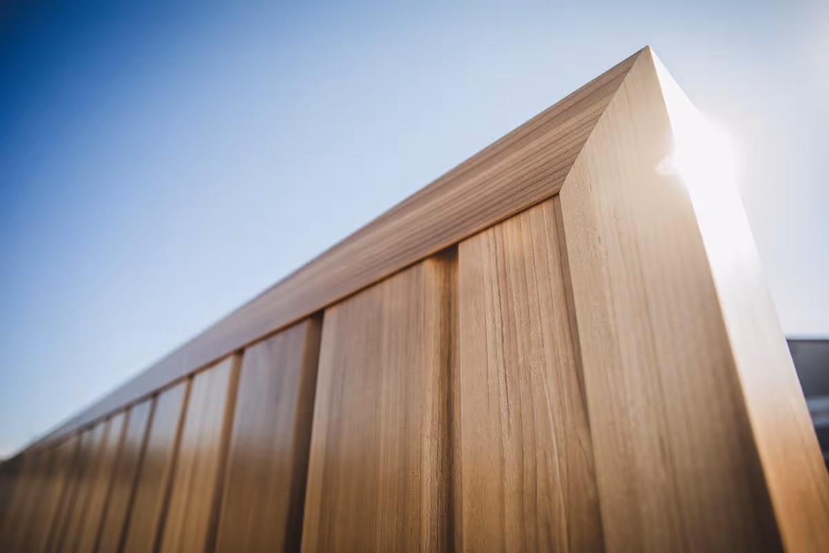Close-up of wooden fence panels under clear blue sky with sunlight shining from the corner.