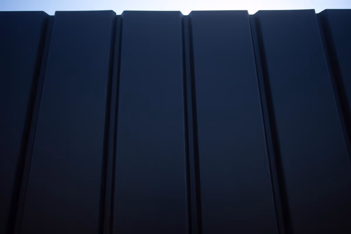Close-up of dark metal fence panels with vertical ridges.