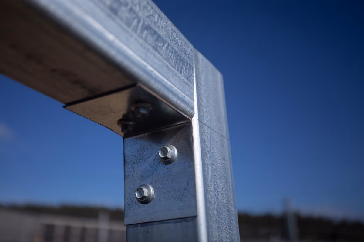 Close-up of a metal fence corner joint with bolts under clear blue sky.