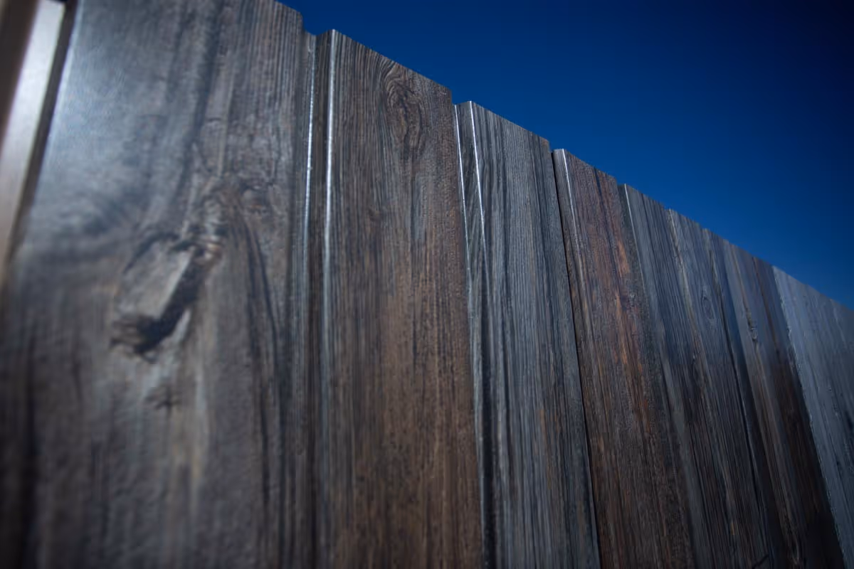 Close-up of dark wooden fence panels under deep blue sky.