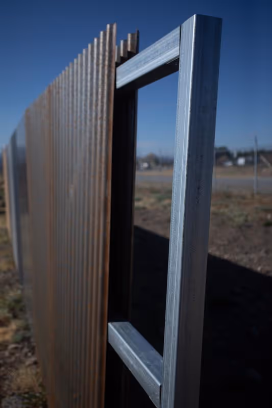 Close-up of metal fence panels with one open gate under a clear blue sky.