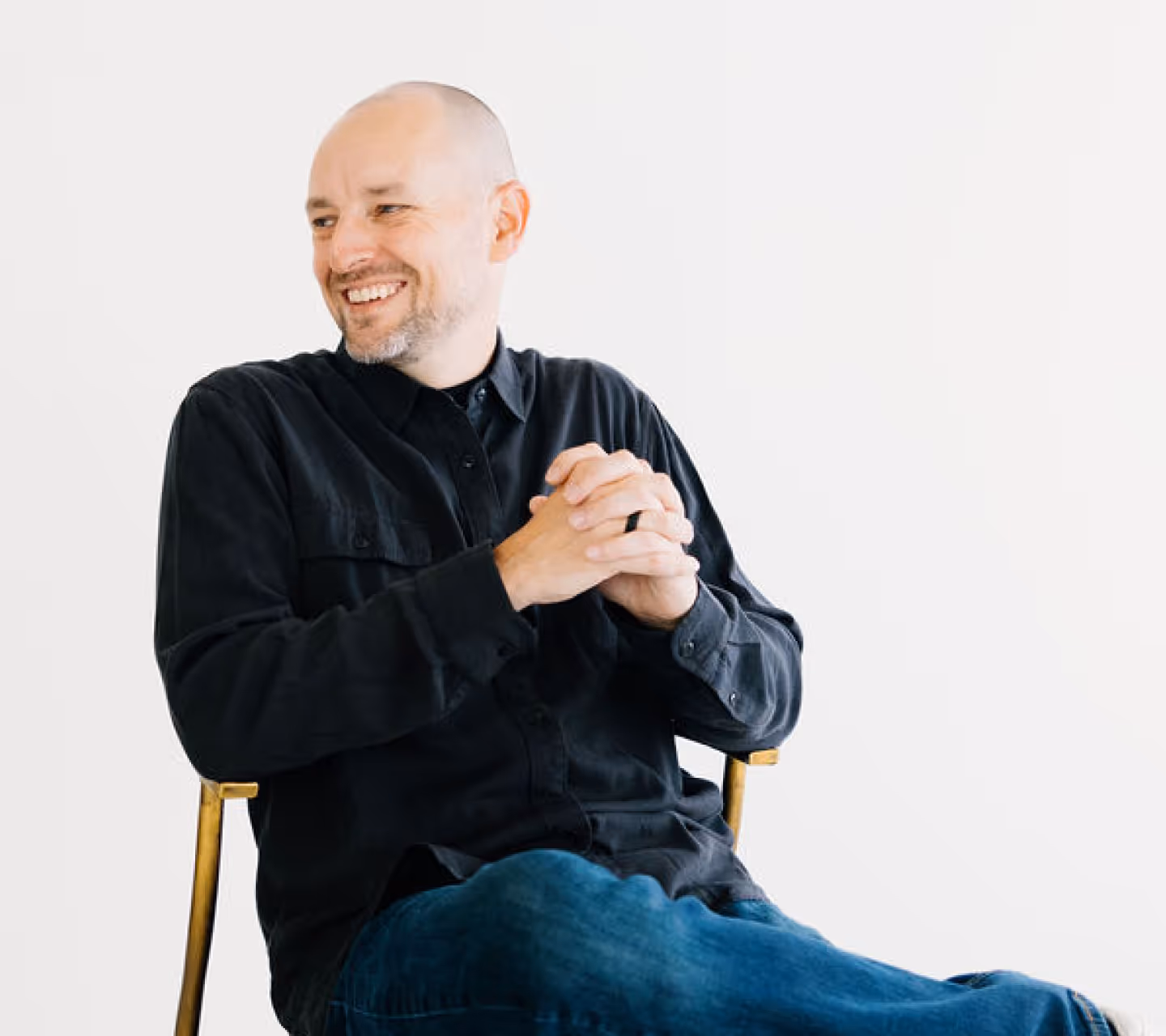 Drew seated in a chair looking over his right shoulder, smiling.