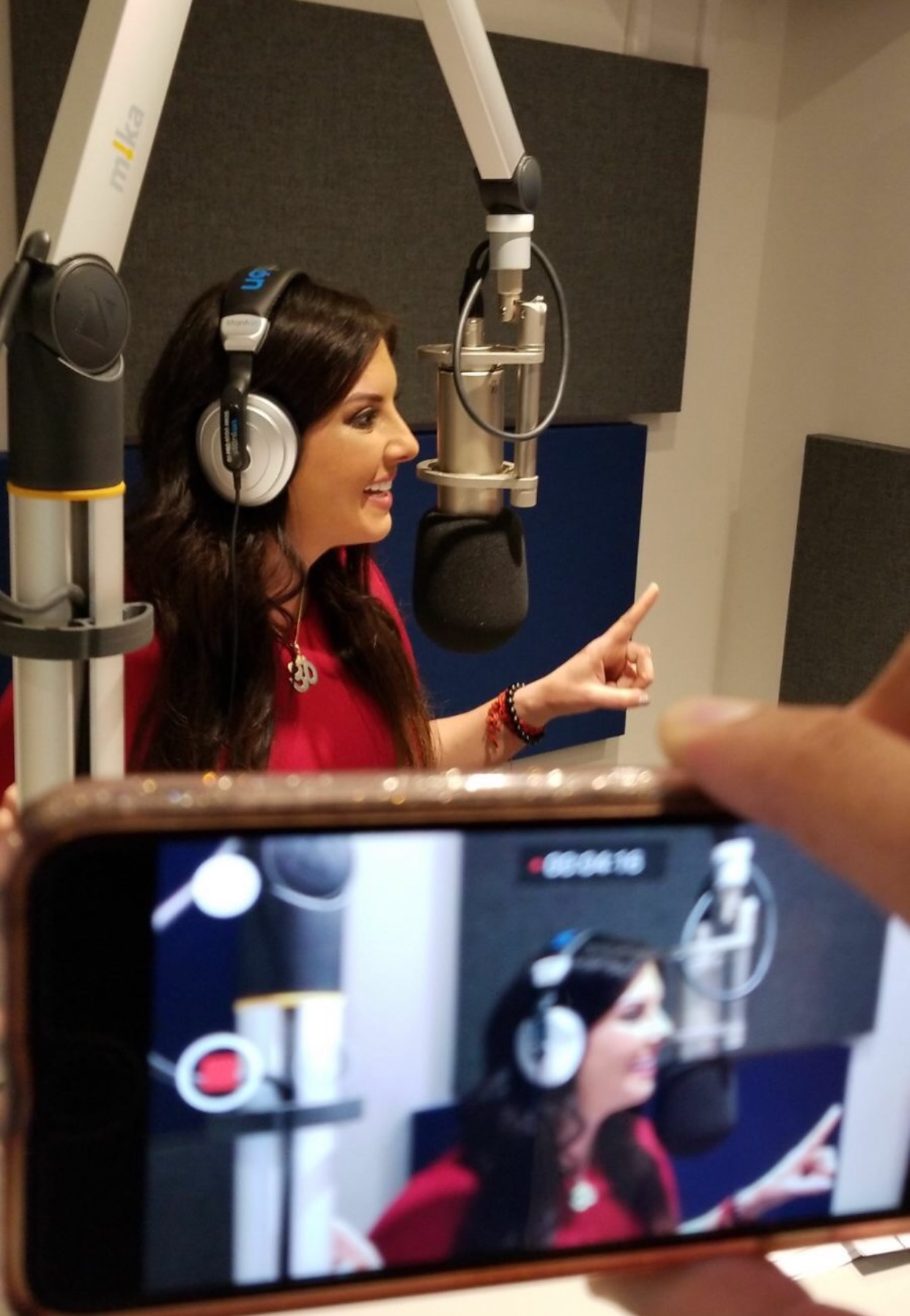 Woman with headphones speaking into a studio microphone, recorded by a smartphone.