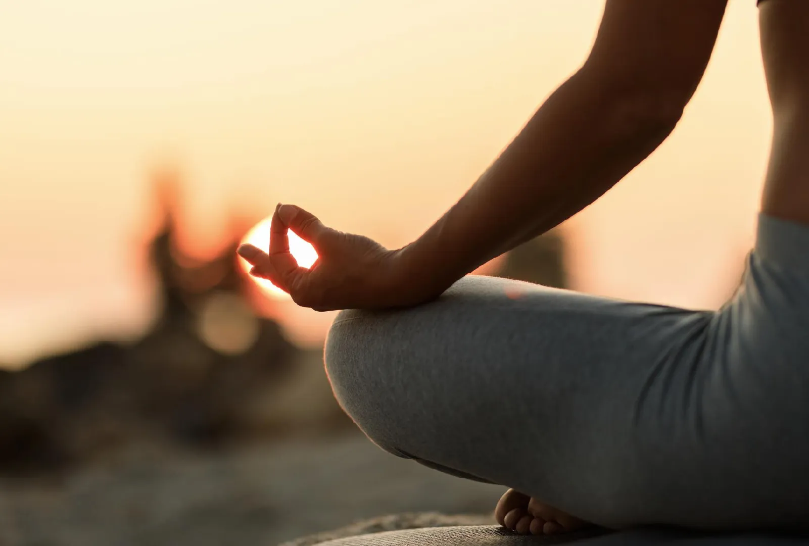 Person meditating outdoors at sunset with hand in a yoga mudra gesture.