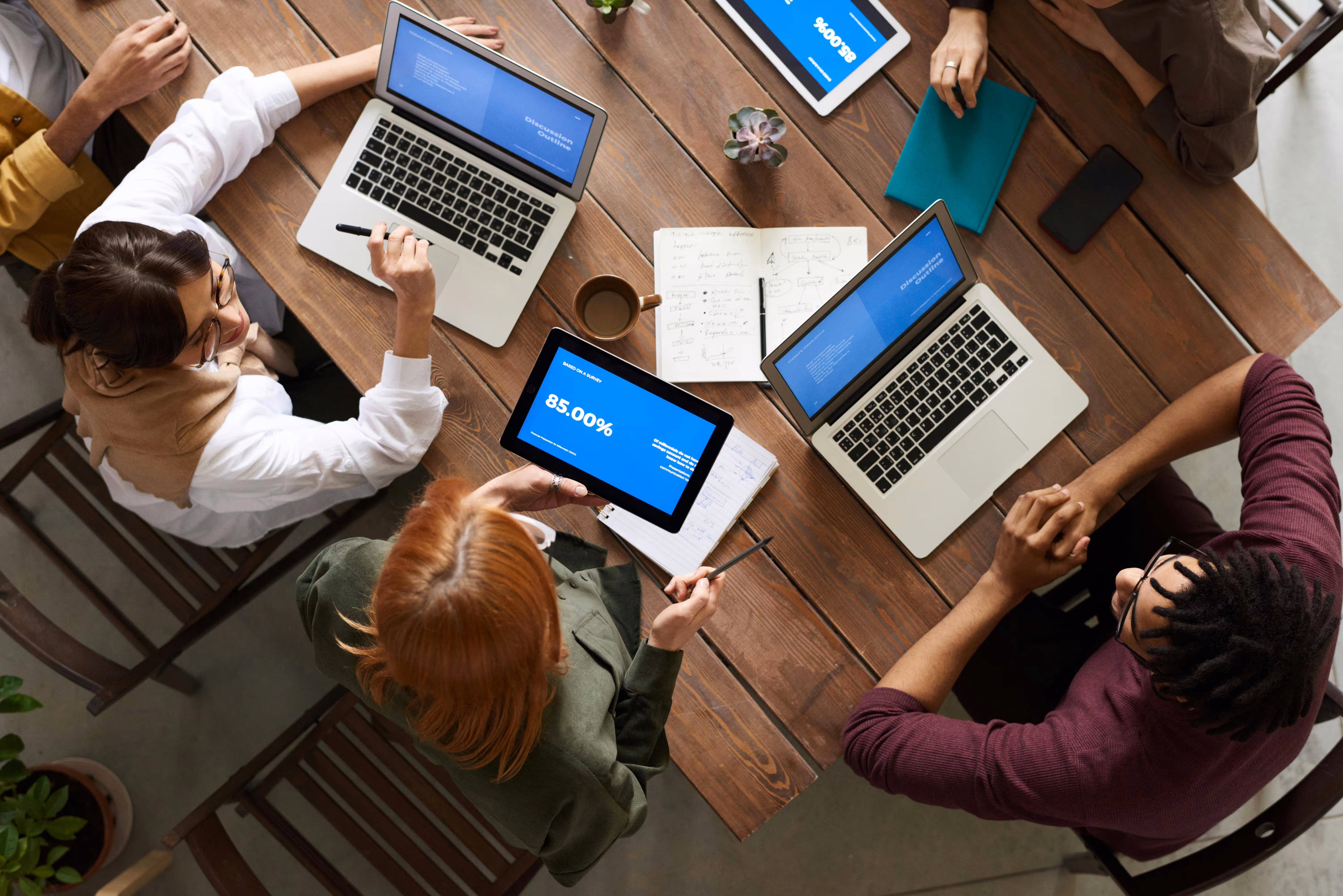 A top-down view of a group of people working on their own individual laptops, but on the same project.