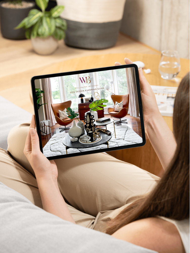 Person holding a tablet displaying the Will Brown Interiors design guide with a styled living room interior on screen.