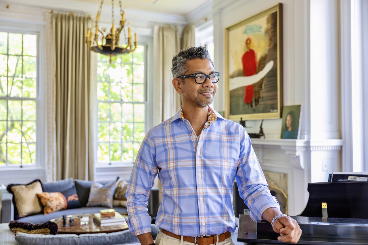 Interior designer Will Brown standing in a bright luxury living room with large windows, chandelier, and curated artwork.