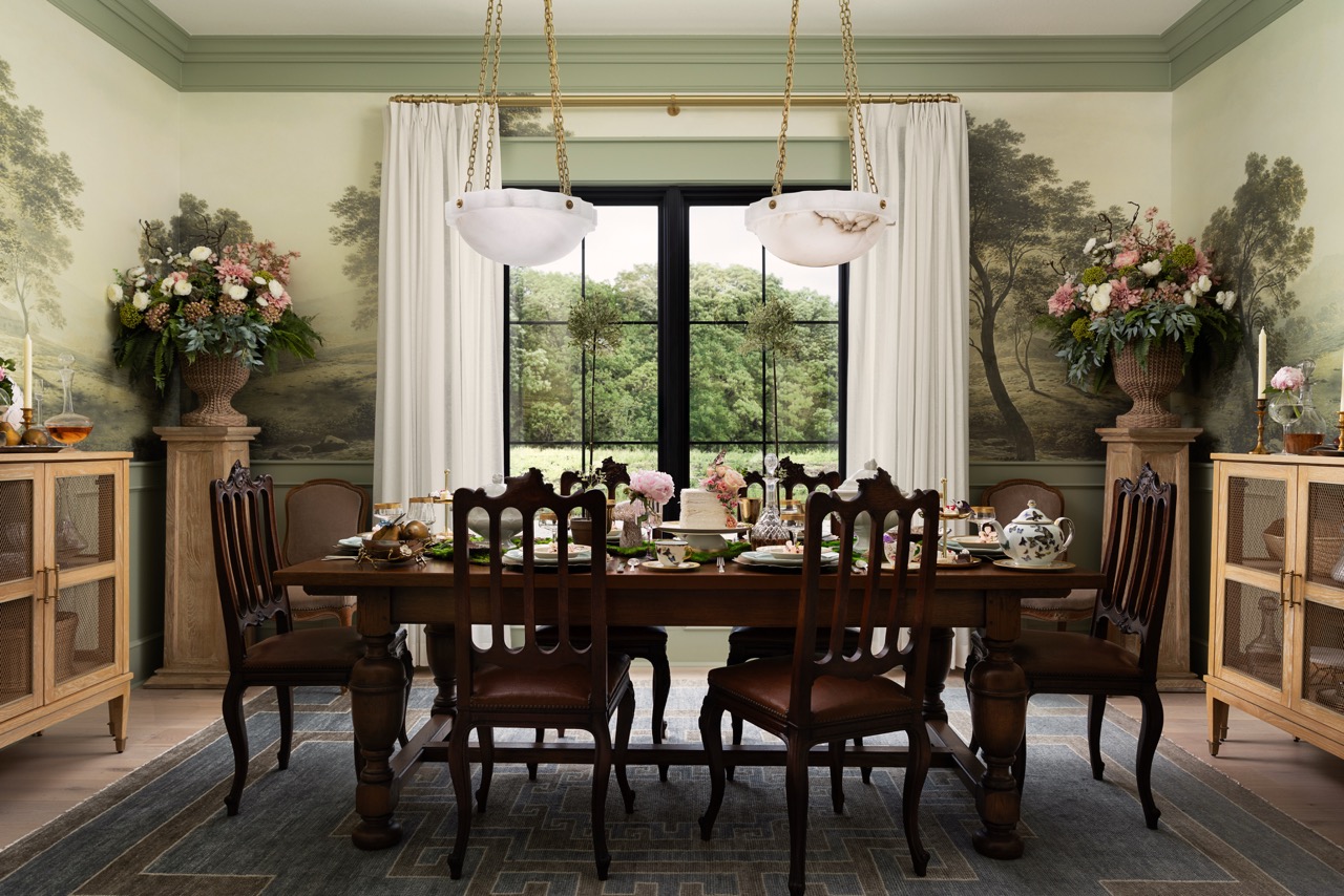 Elegant dining room with landscape wall mural, dark wood table, floral arrangements, and hanging pendant lights.