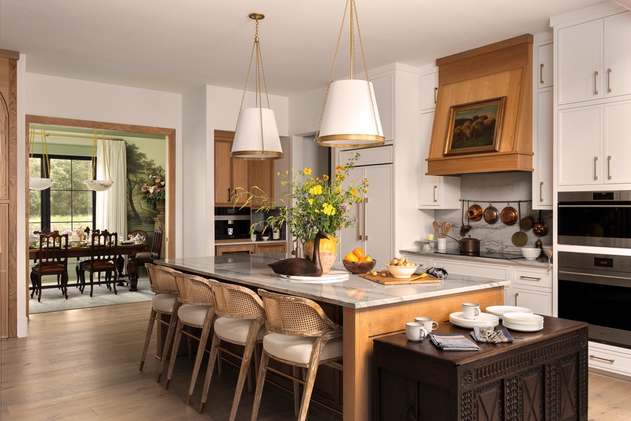 Bright kitchen with marble island, cane bar stools, brass pendant lights, and white cabinetry.