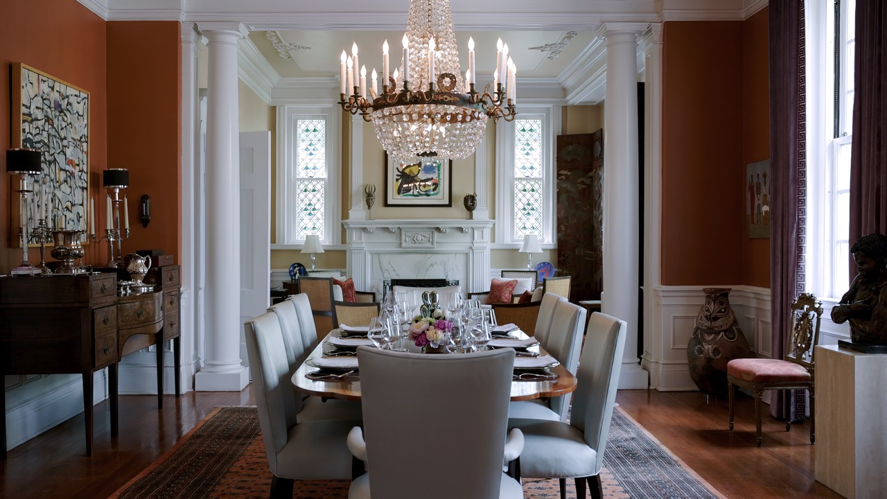 Formal dining room with long table, white columns, crystal chandelier, and classic architectural details.