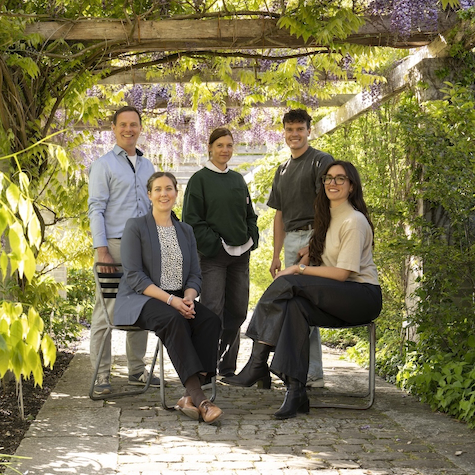 Das Team der Geschäftsstelle des Vereins Grünes Gallustal sitzt und steht unter einem blühenden Pergola-Rosenbogen an einem sonnigen Tag.