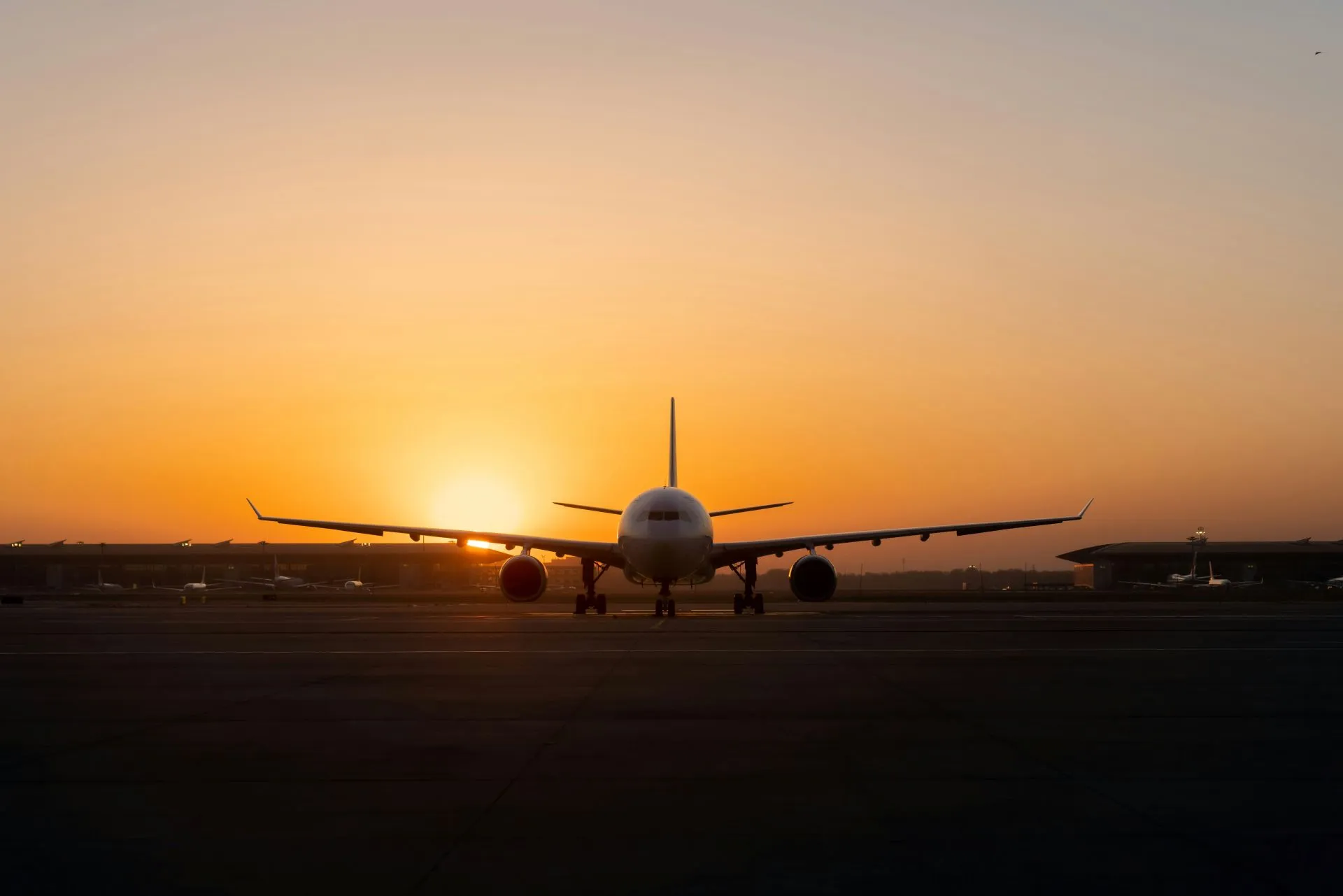 Front view of a large airplane on the runway with the sun setting behind it at an airport.