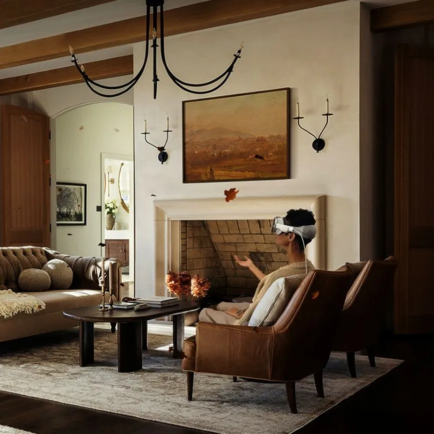 Person wearing virtual reality headset sitting in leather chair in cozy living room with fireplace and autumn decor.